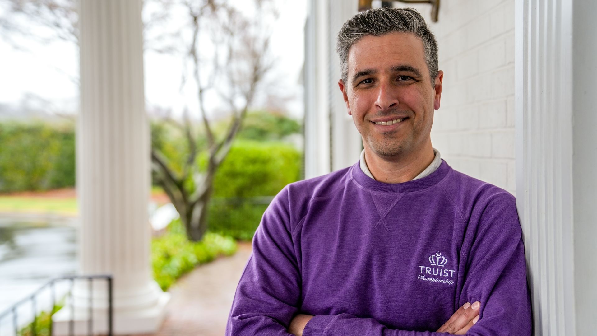 Truist Championship director in a purple crew neck jumper stands next to the entrance at Quail Hollow Club. 