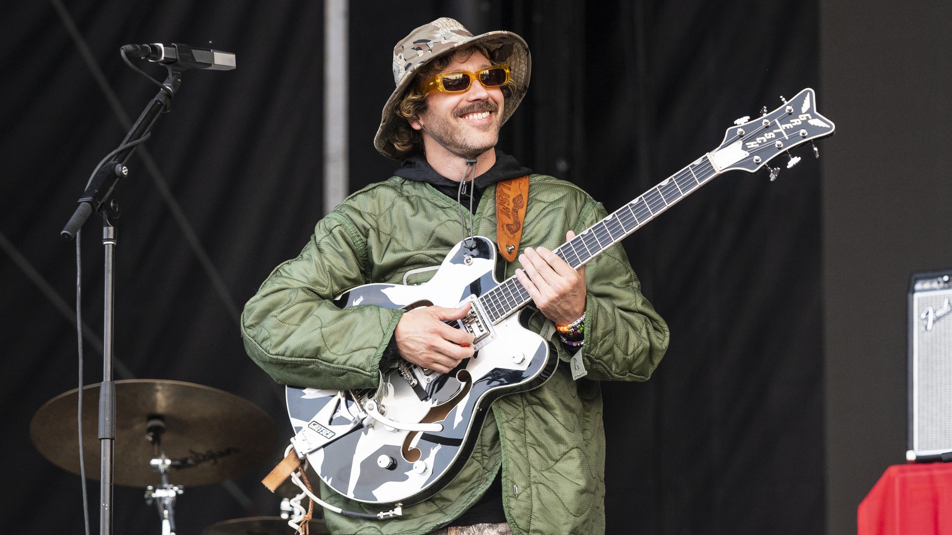 man wearing a bucket hat smiles while holding a guitar