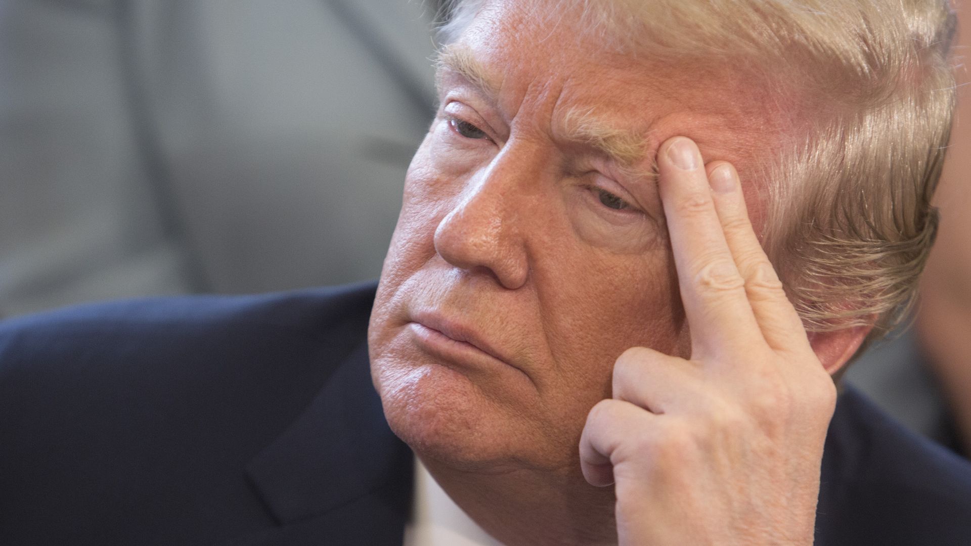 A closeup of Donald Trump looking concerned and looking to the side with two fingers pressed against the side of his forehead