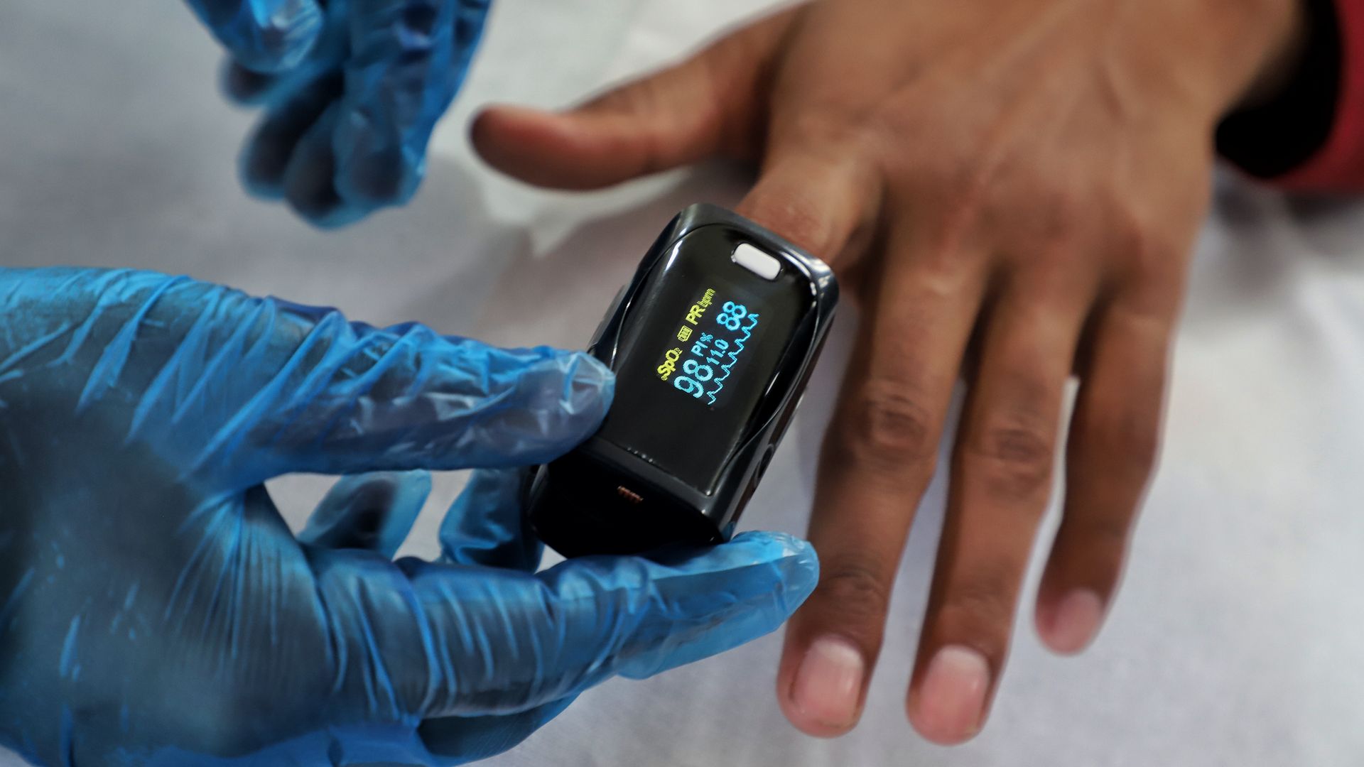 A photo of a health worker holding a pulse oximeter on a patient's finger.