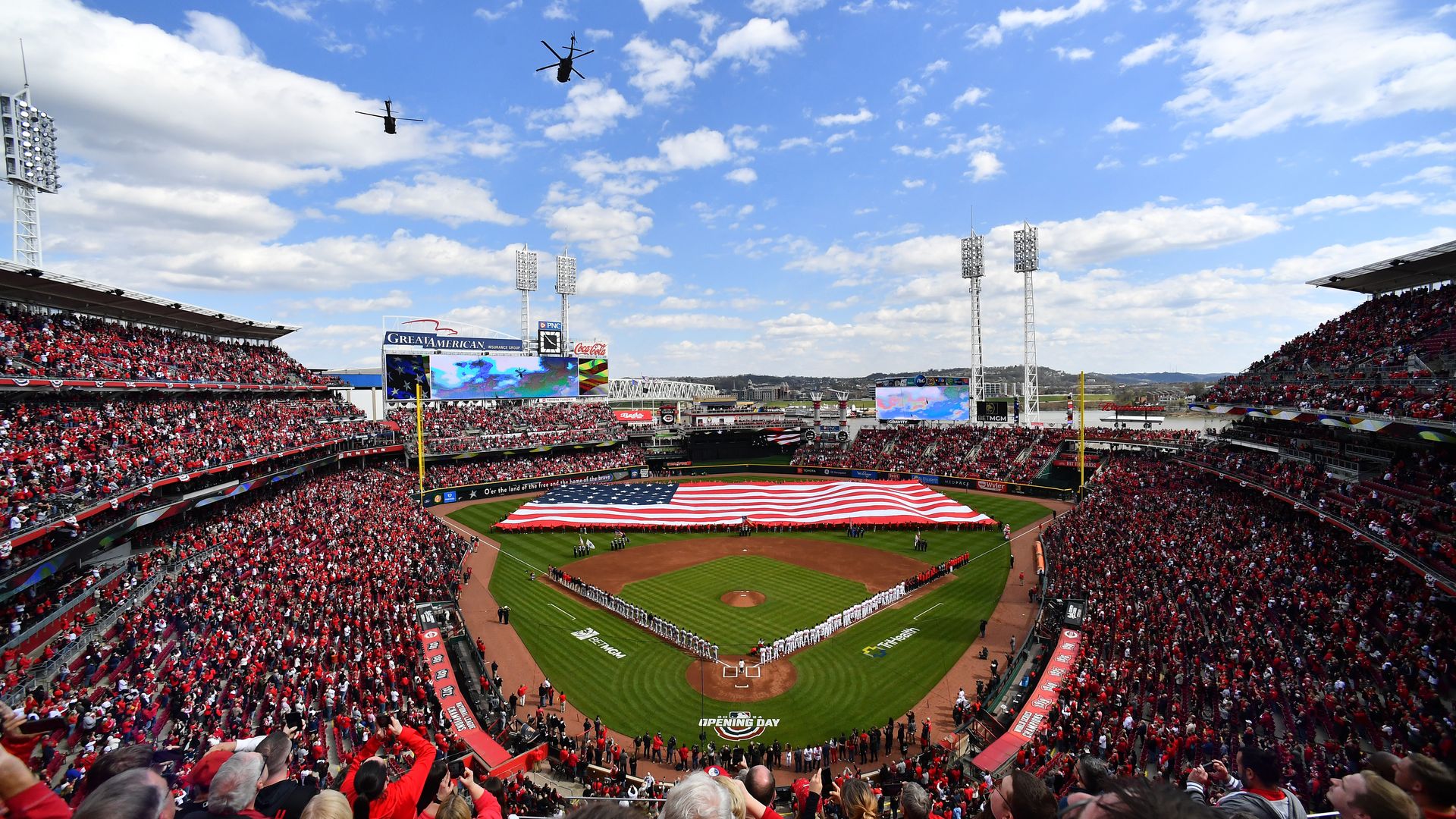 An overhead view of Great American Ballpark in Cincinnati, with a large U.S. flag unfurled in the outfield. 