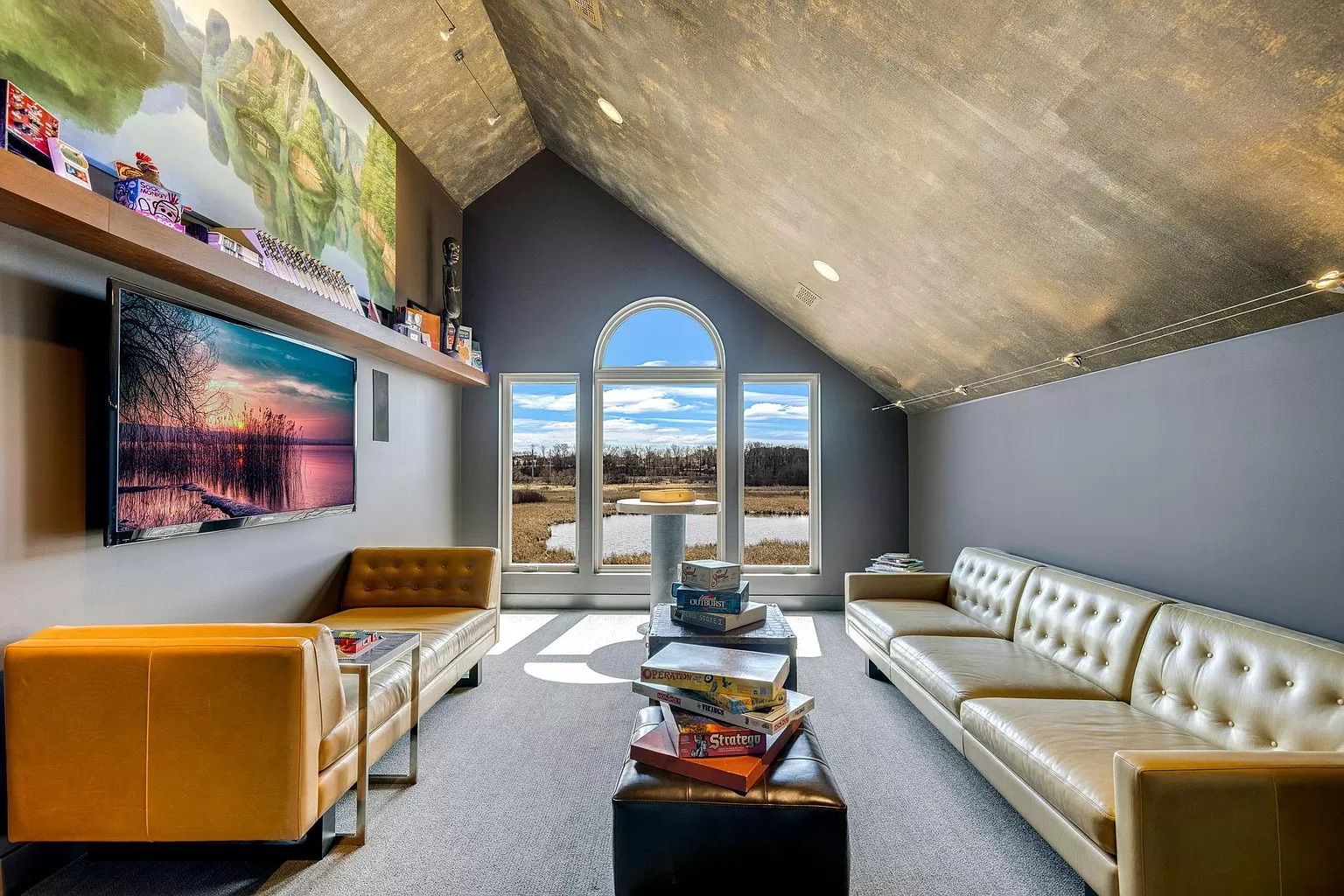 A room with gray walls and a television with multiple board games on the wall.