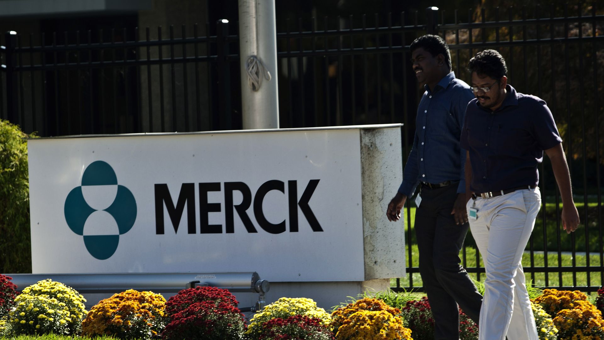 Two people walking outside of a building with a Merck sign.