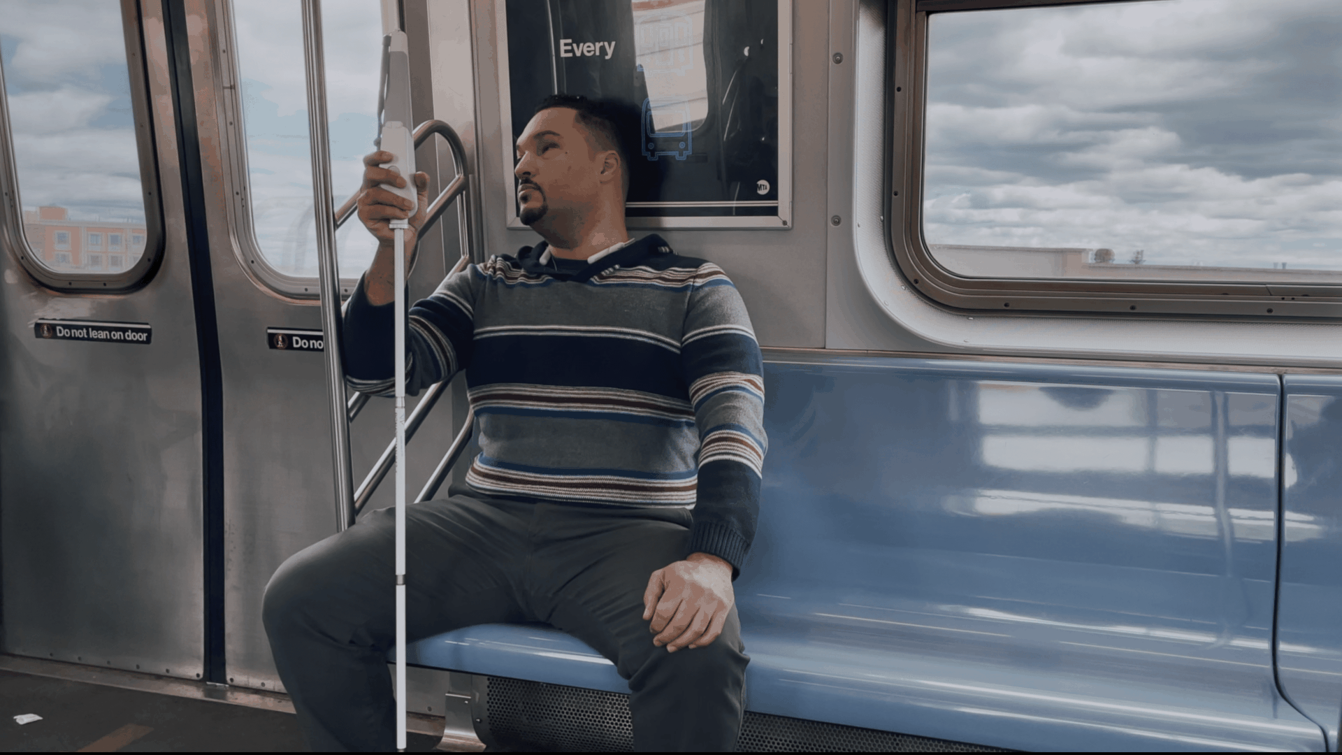 Image of a visually impaired man with a WeWalk "smart cane" riding the subway.
