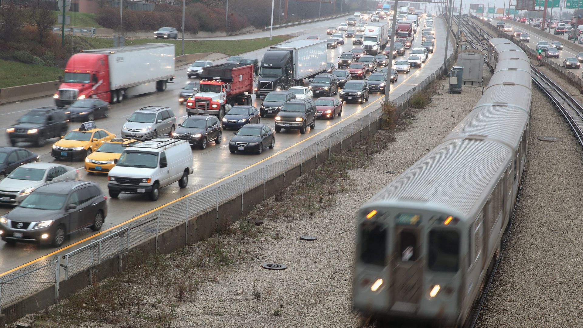 Photo of traffic on a road with a train whizzing by. 