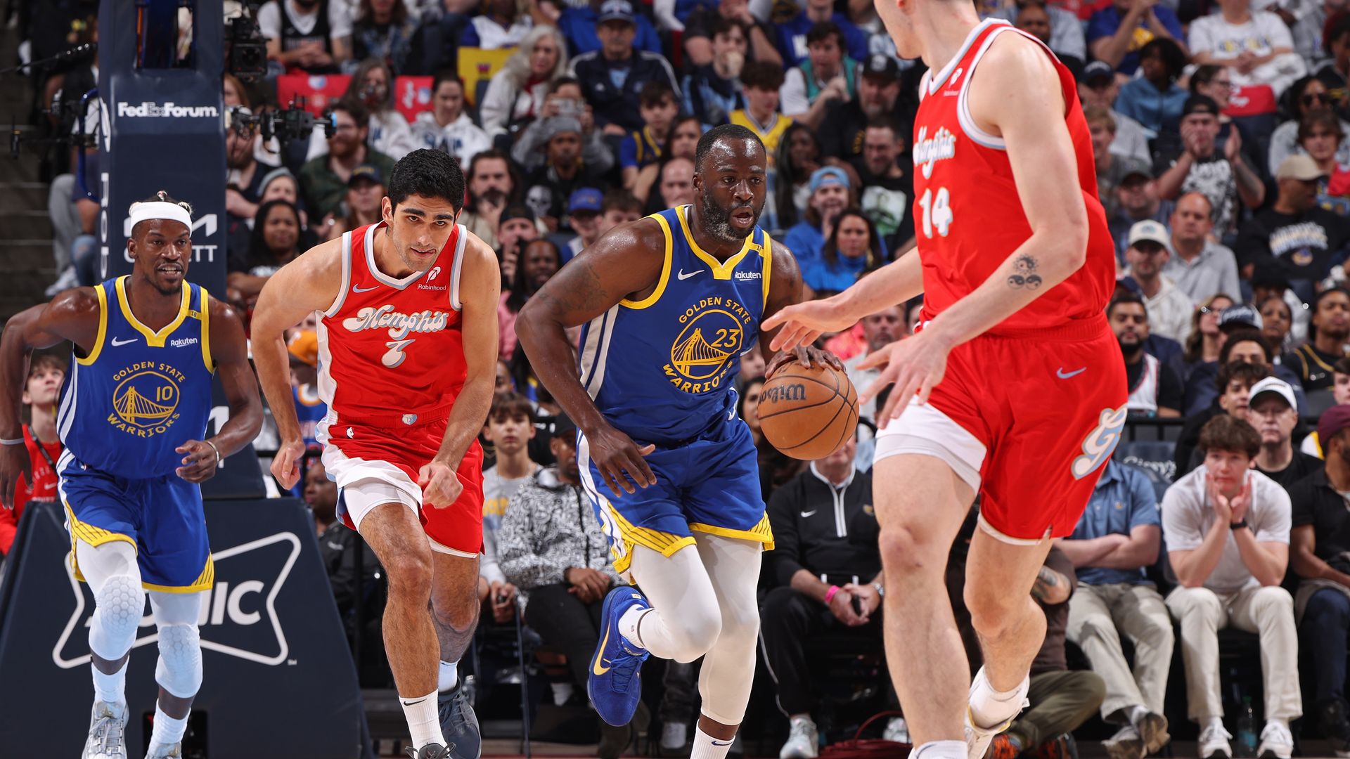 A man in a blue basketball uniform dribbles against players wearing red