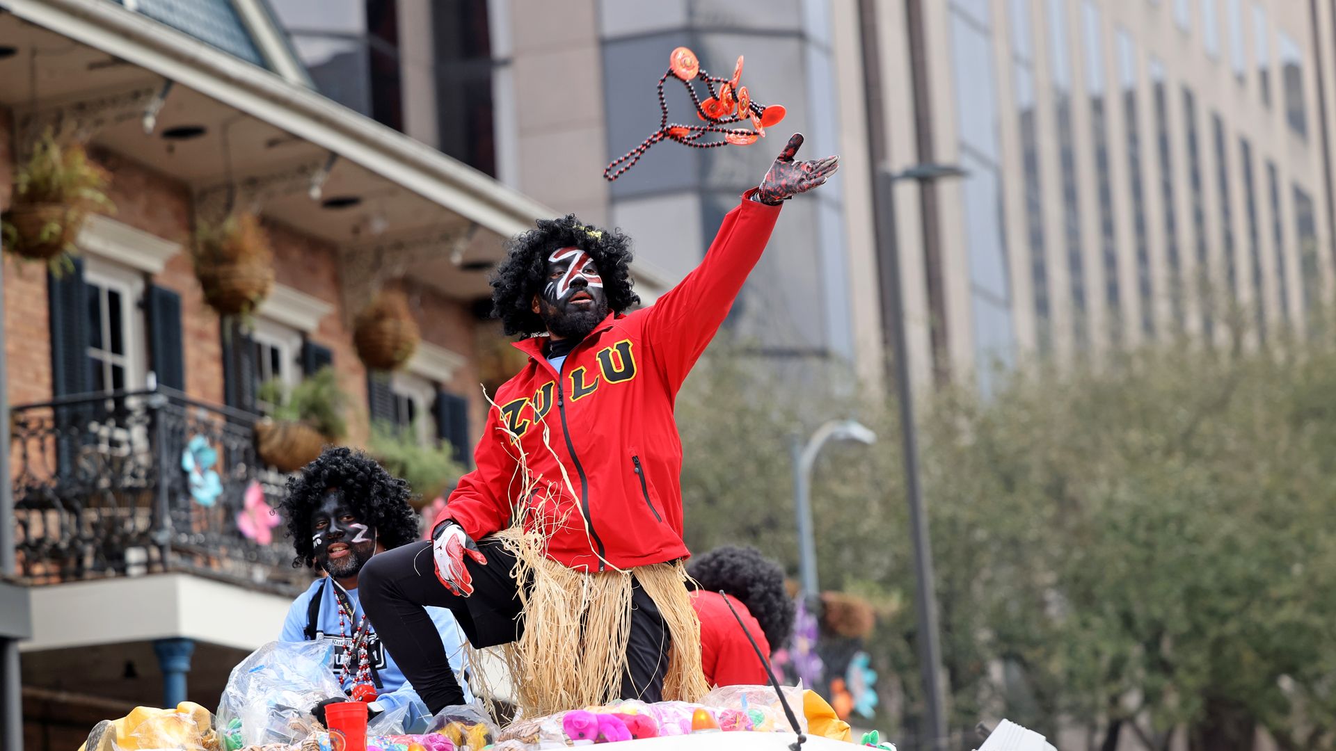 A person wearing a Zulu sweater tosses beads into the air while riding on top of a firetruck.