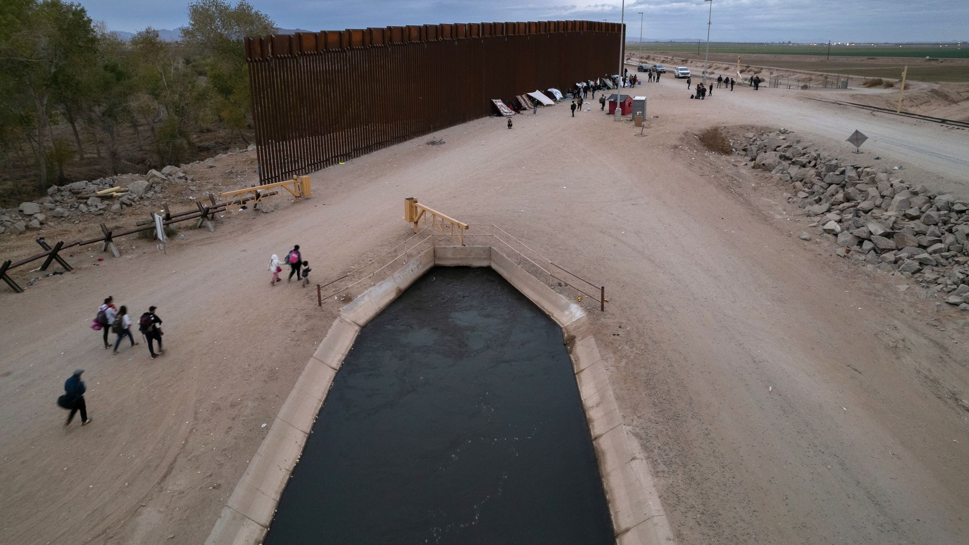 In an aerial view, Immigrants walk towards a makeshift encampment along the U.S. border wall after crossing from Mexico through a gap in the structure on December 10, 2021 in Yuma, Arizona