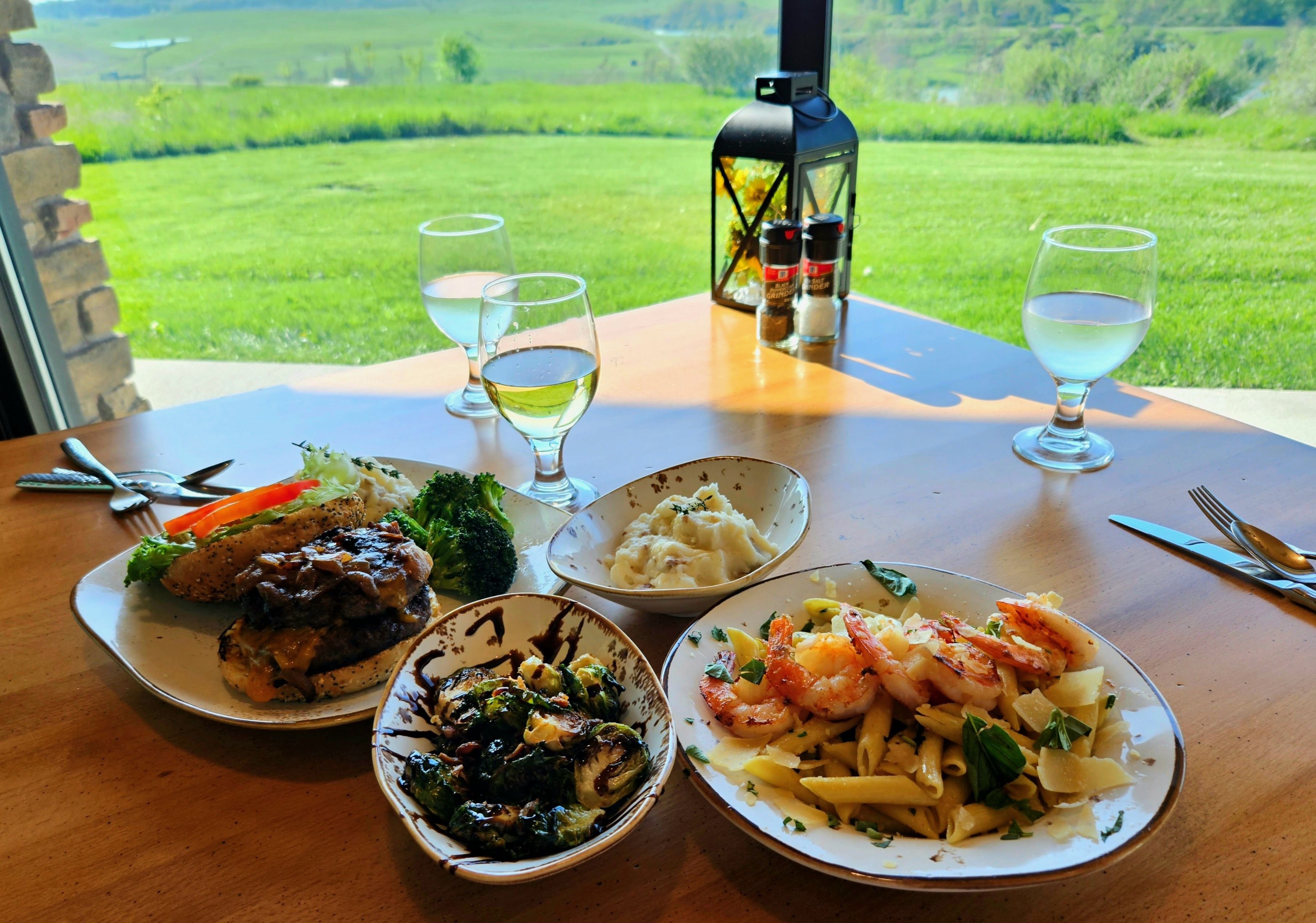 Two plates of food with wine glasses on a table overlooking green hills