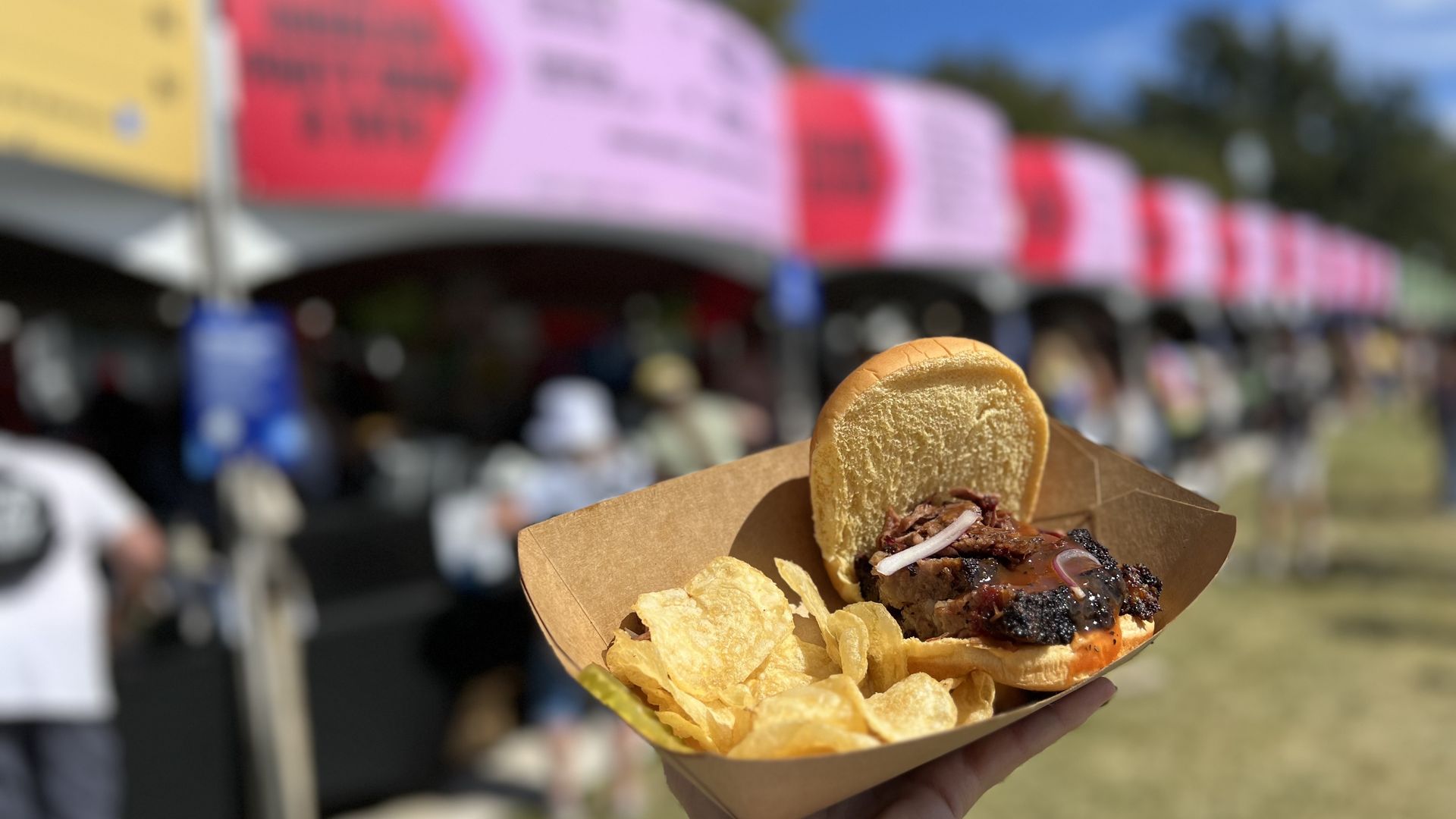 A photo of a burger and chips on a plate with food signage in the background