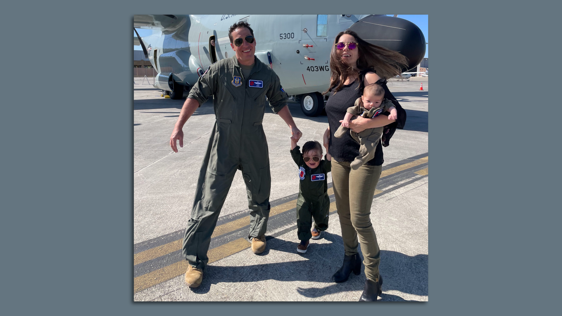 Photo shows the Gharby family smiling in front of a Hurricane Hunter WC-130. Dad and the two children are wearing matching flight suits.