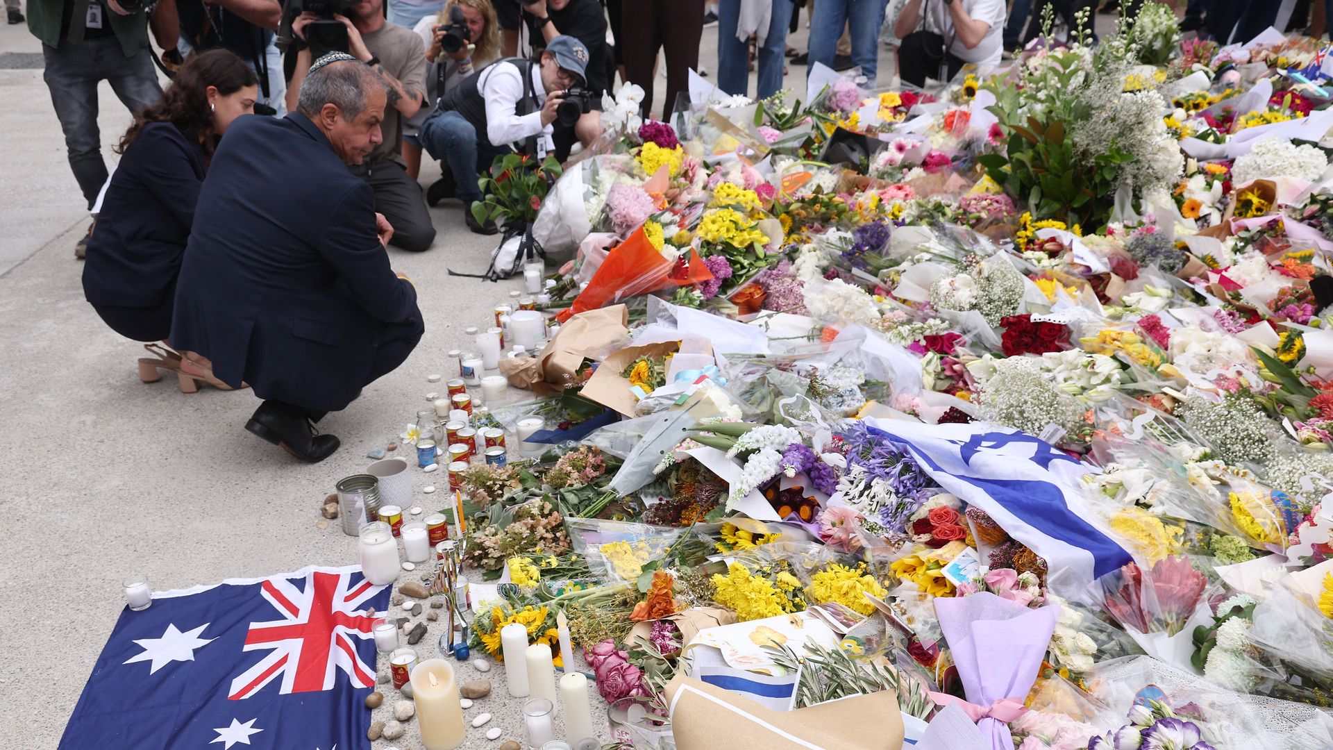 Israeli Ambassador to Australia Amir Maimon (L), wearing a dark scull cap and navy suit, crouches down as he looks at a sea of floral tributes to the victims of the Bondi Beach mass shooting in Sydney, Australia.