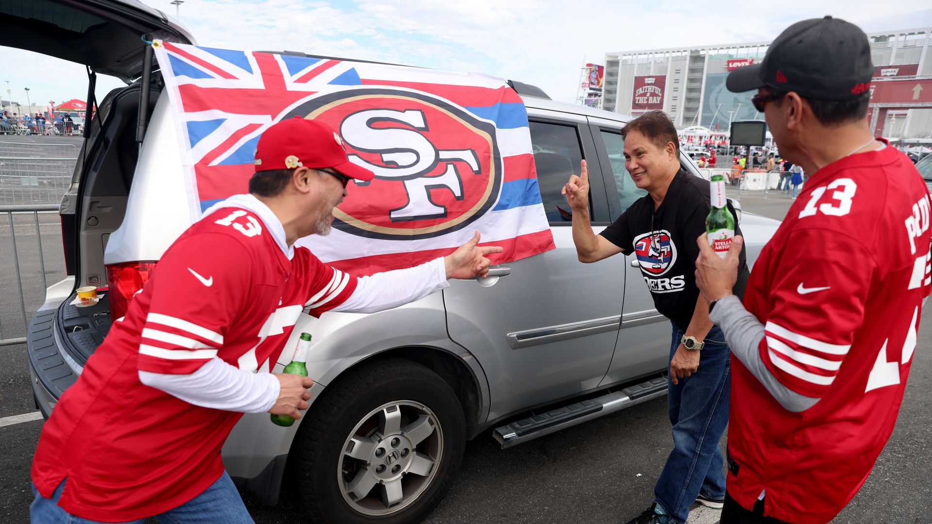Photo of SF 49er fans standing next to a minivan with a Hawaiian flag that has the 49ers logo
