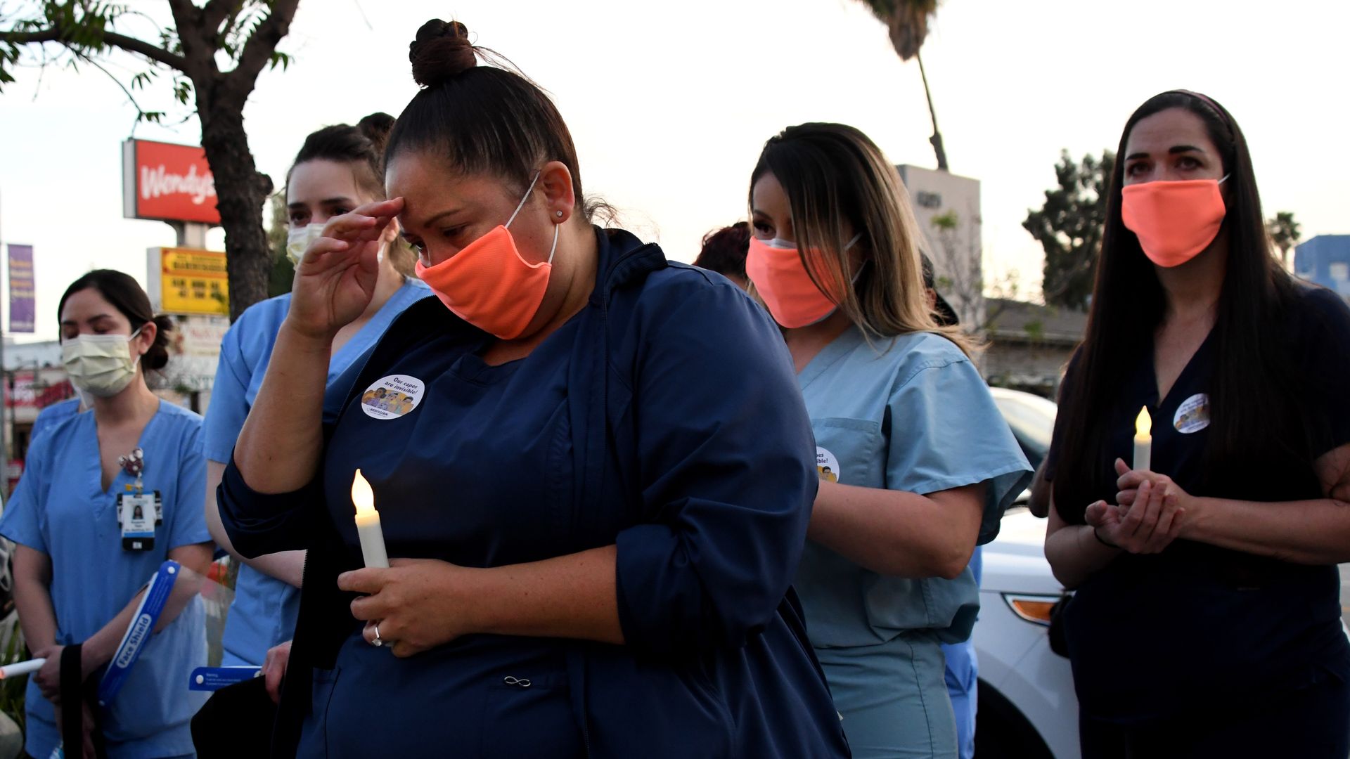 Nurses in scrubs and masks hold a memorial outside a hospital.