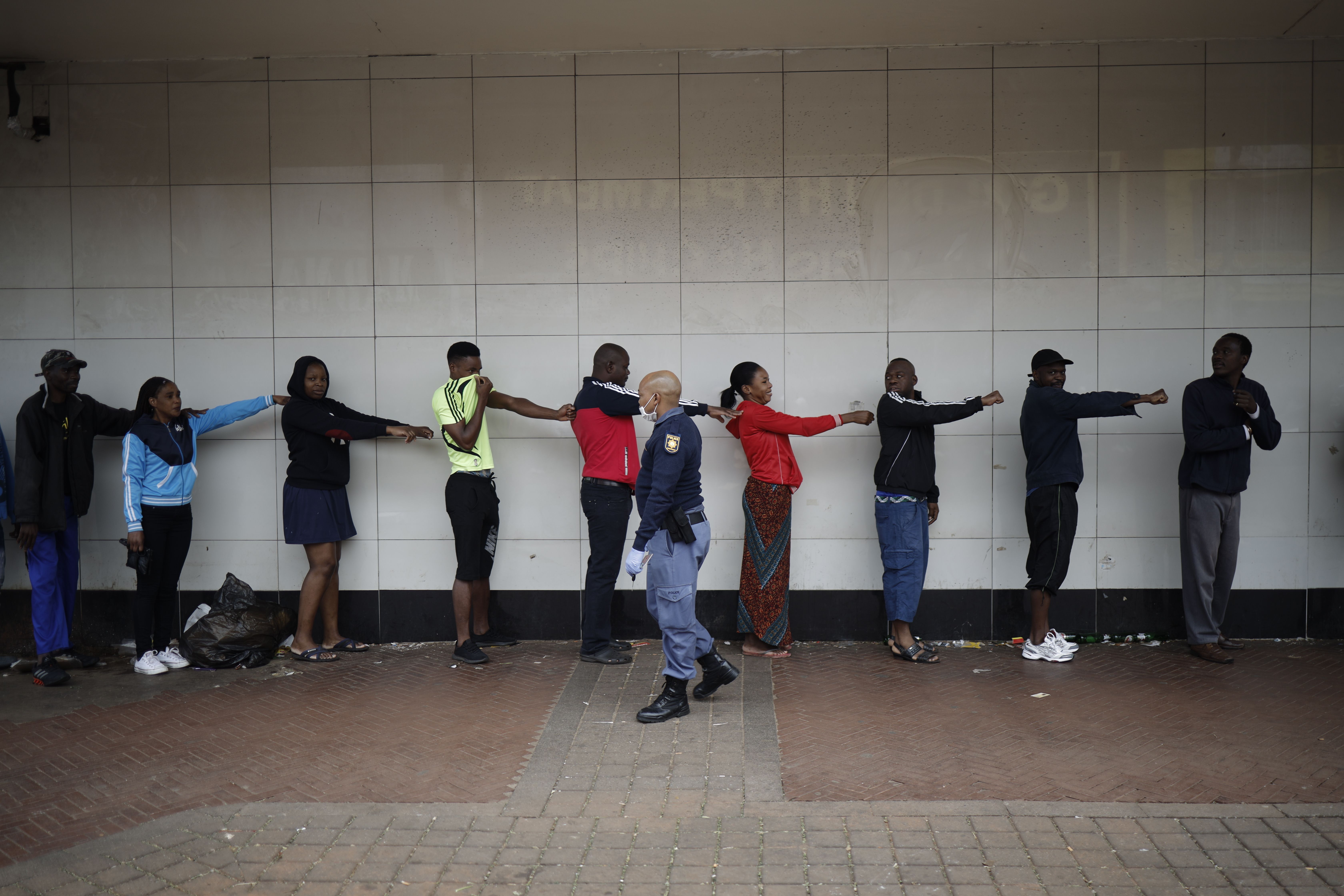 A member of the South African Police Service (SAPS) enforces social distancing as he makes shoppers hold their hands out in front of them