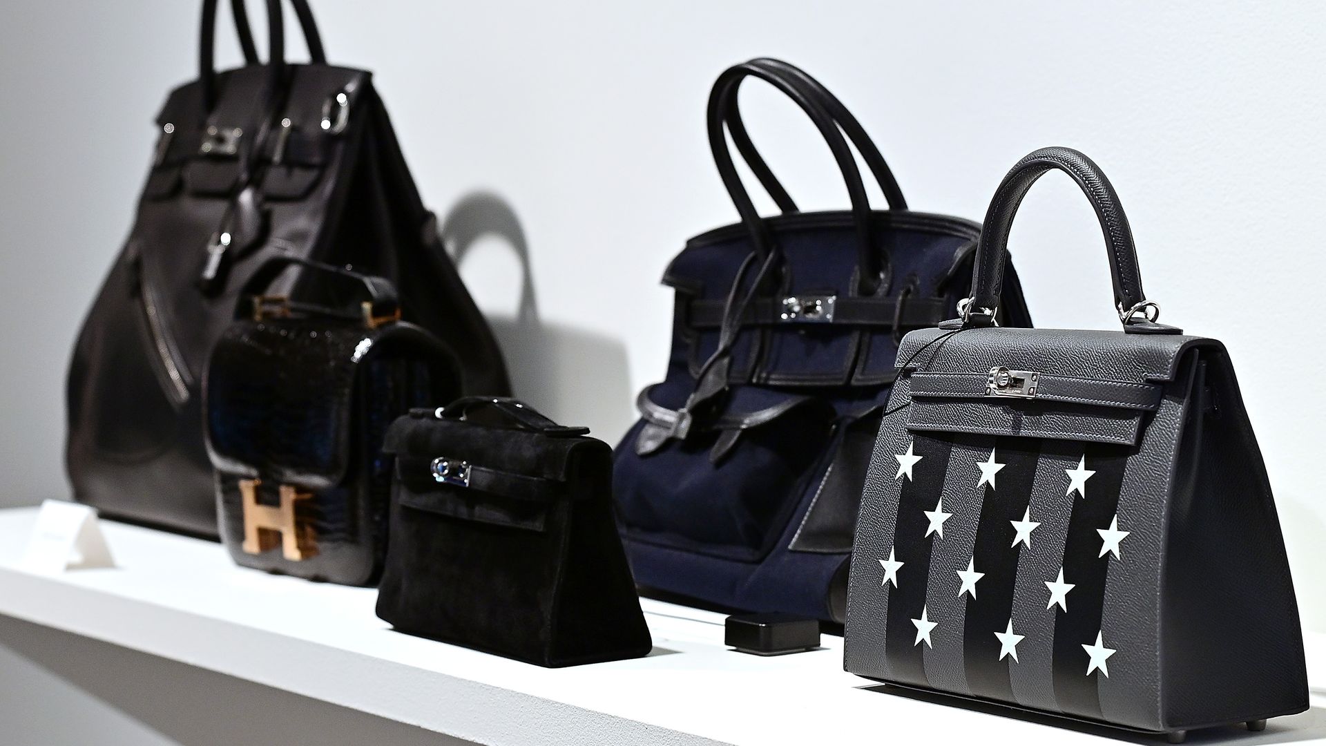 Four black handbags sitting on a white shelf