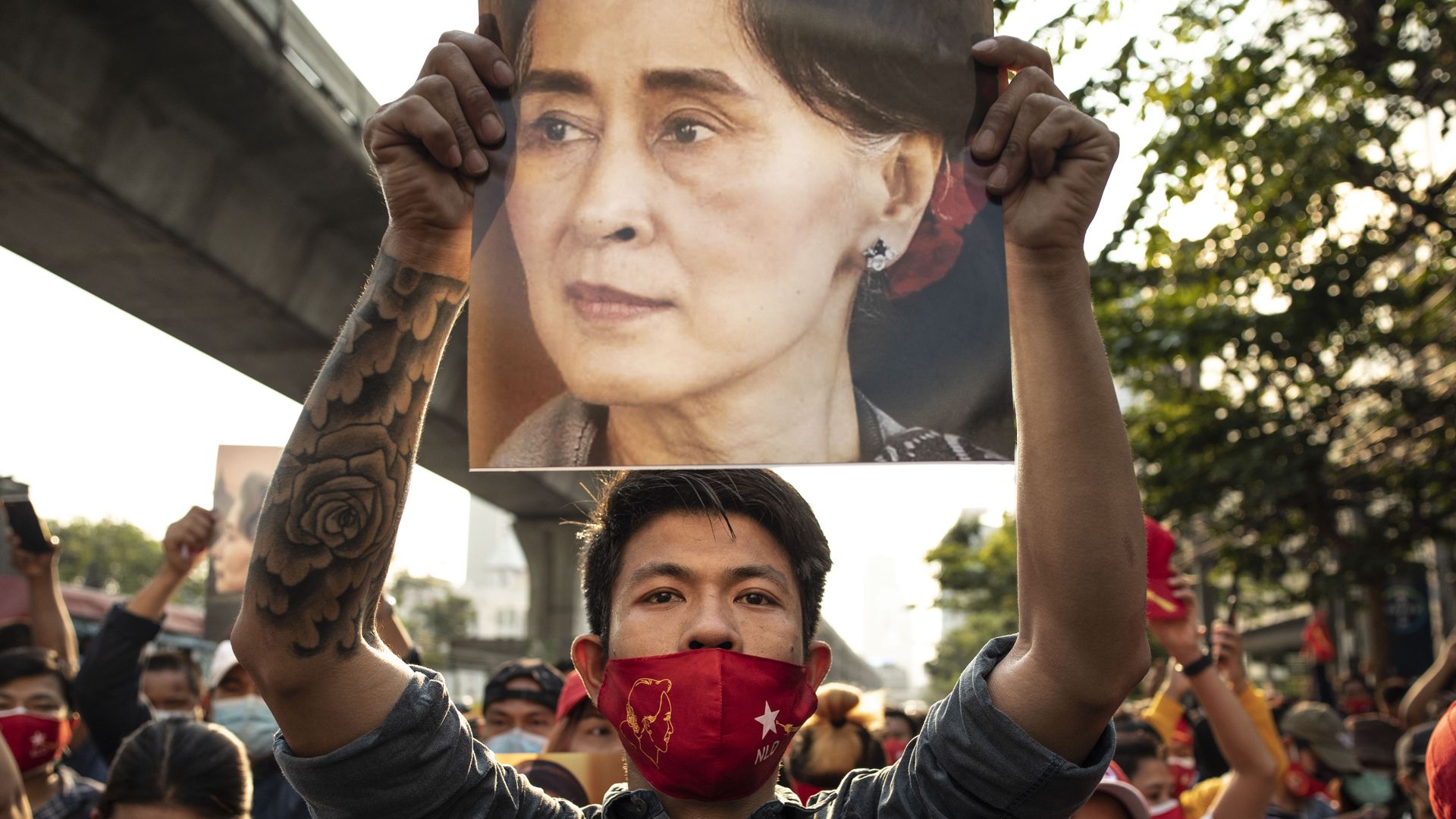 Picture of a young man in a protest in Myanmar holding a poster of Aung San Suu Kyi
