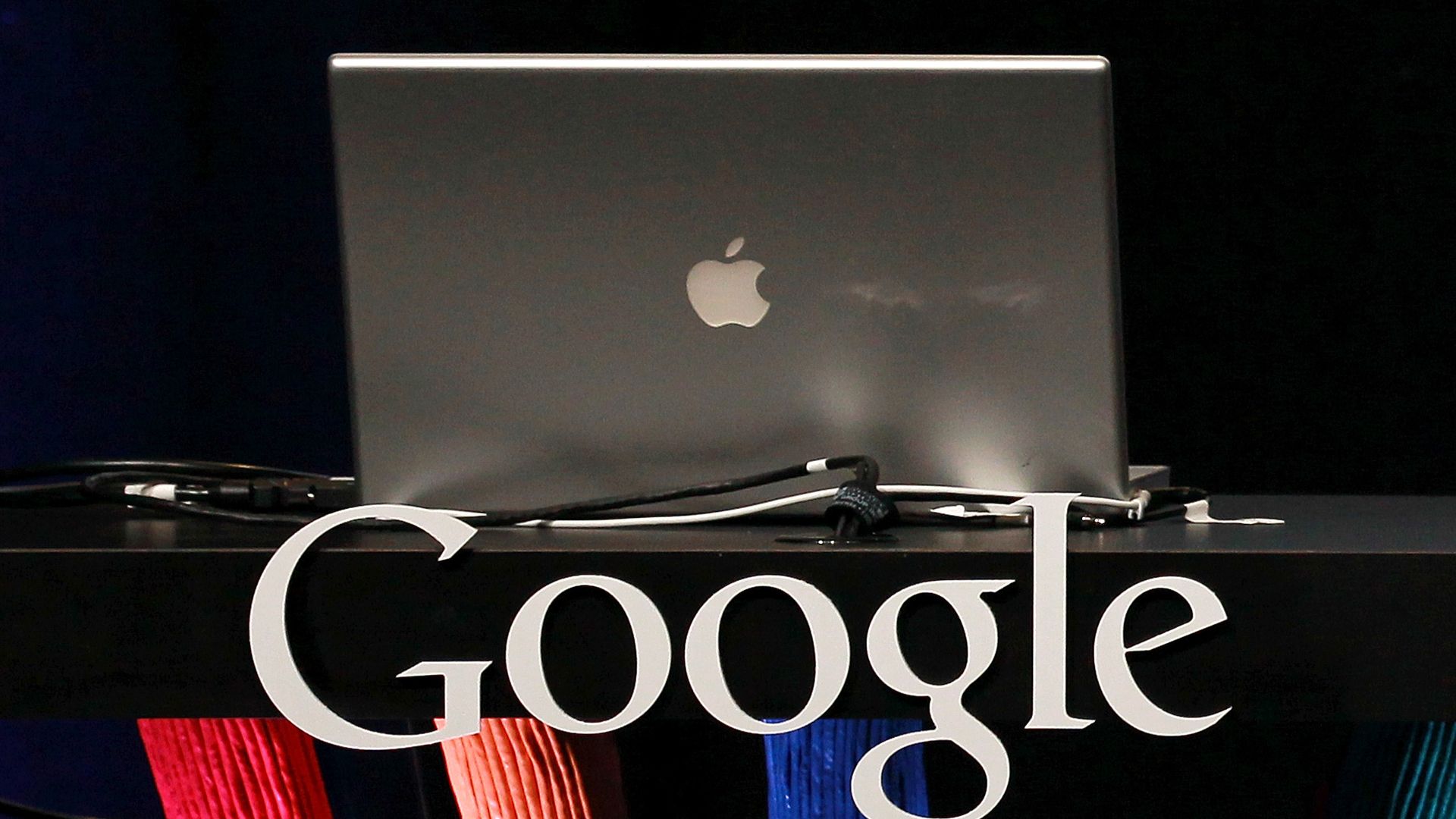 The Google logo underneath an Apple laptop.