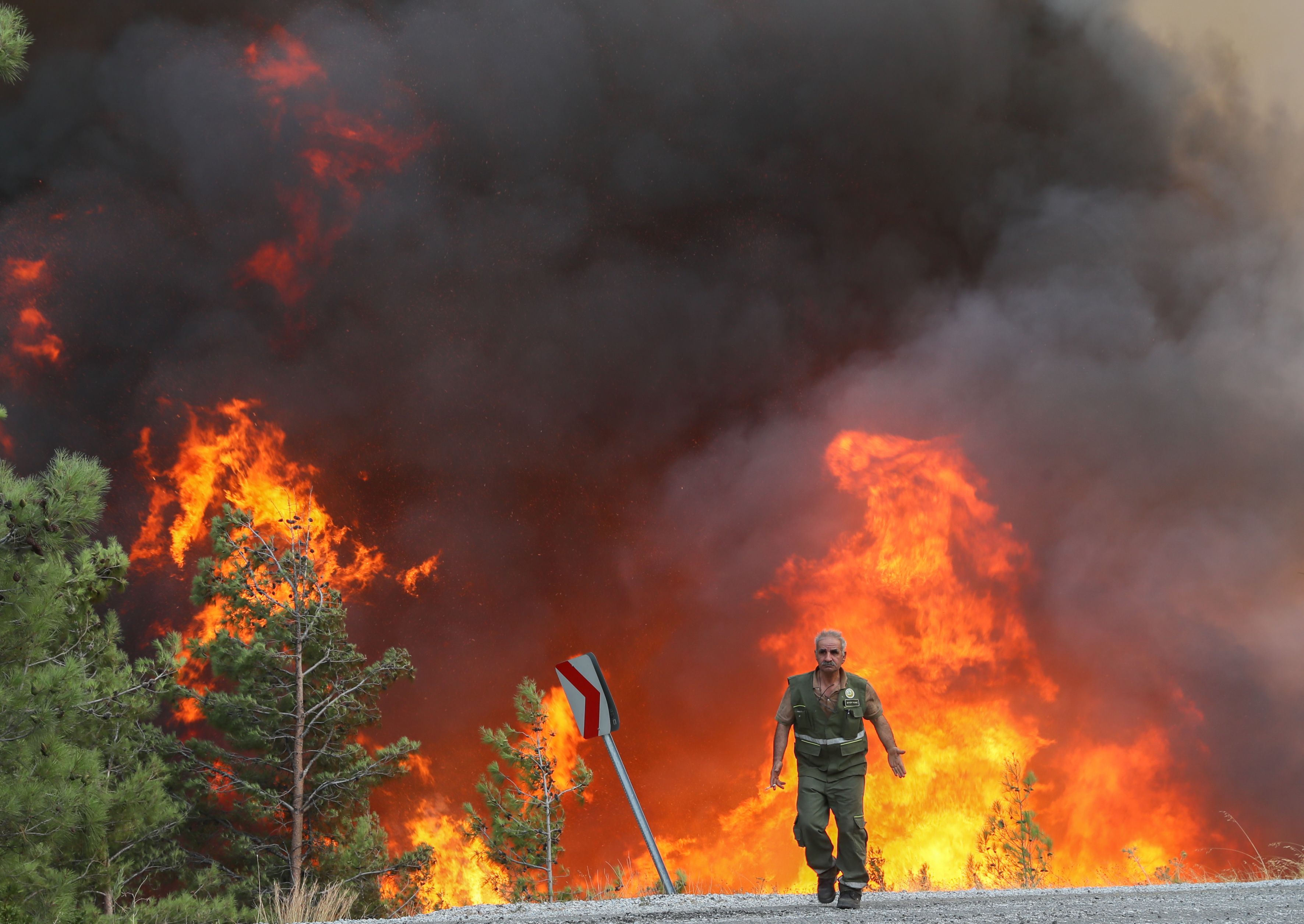 A man in uniform walks on a road in front of a billowing fire in Turkey