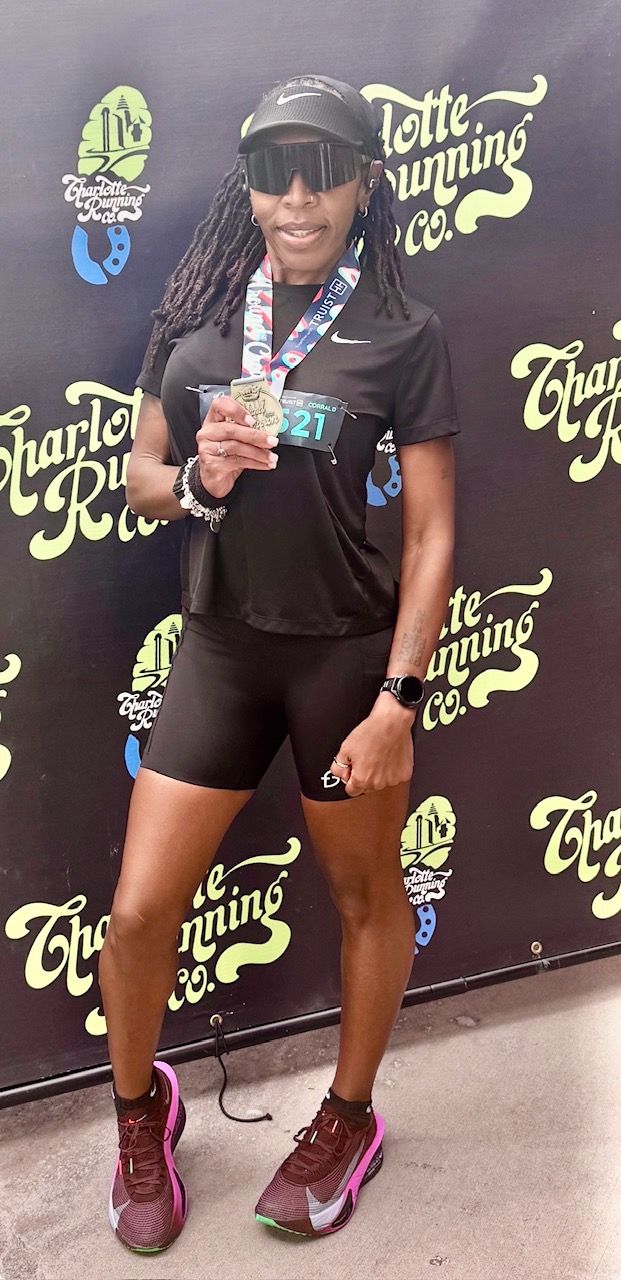 Runner posing in front of a sign holding a medal. 