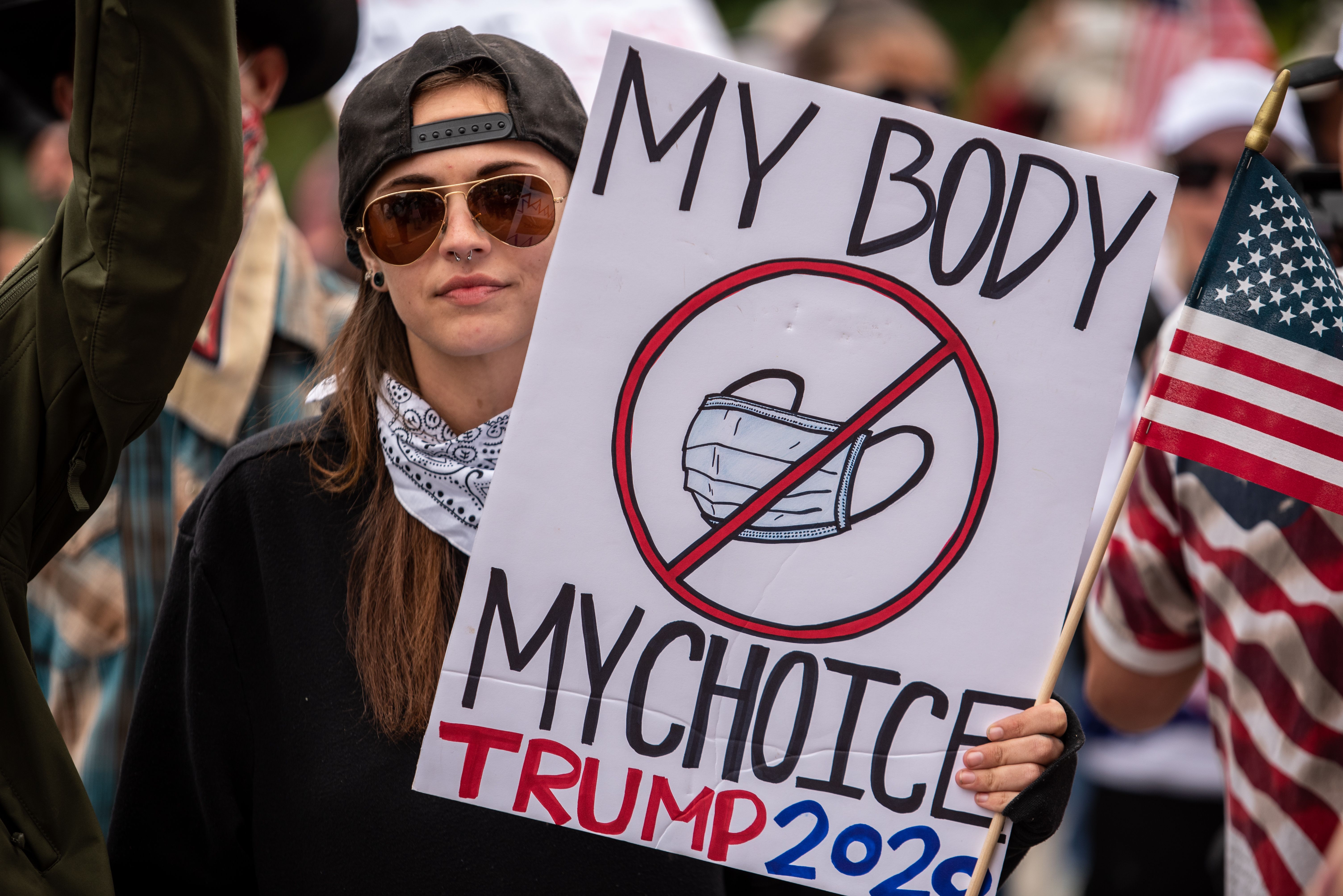 In this image, a woman holds a sign that reads "My body my choice" with a drawing of a face mask crossed out