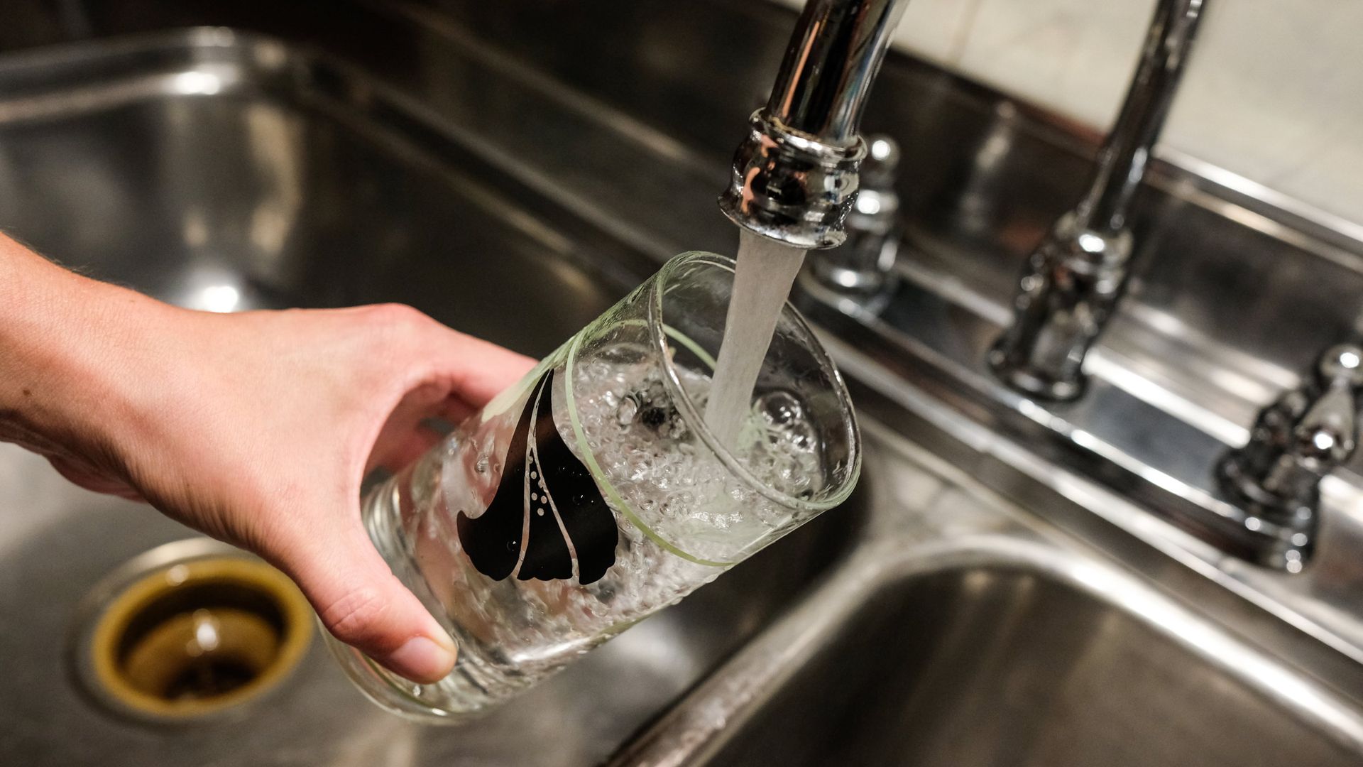 Hand holding a glass of water as it fills from a kitchen faucet