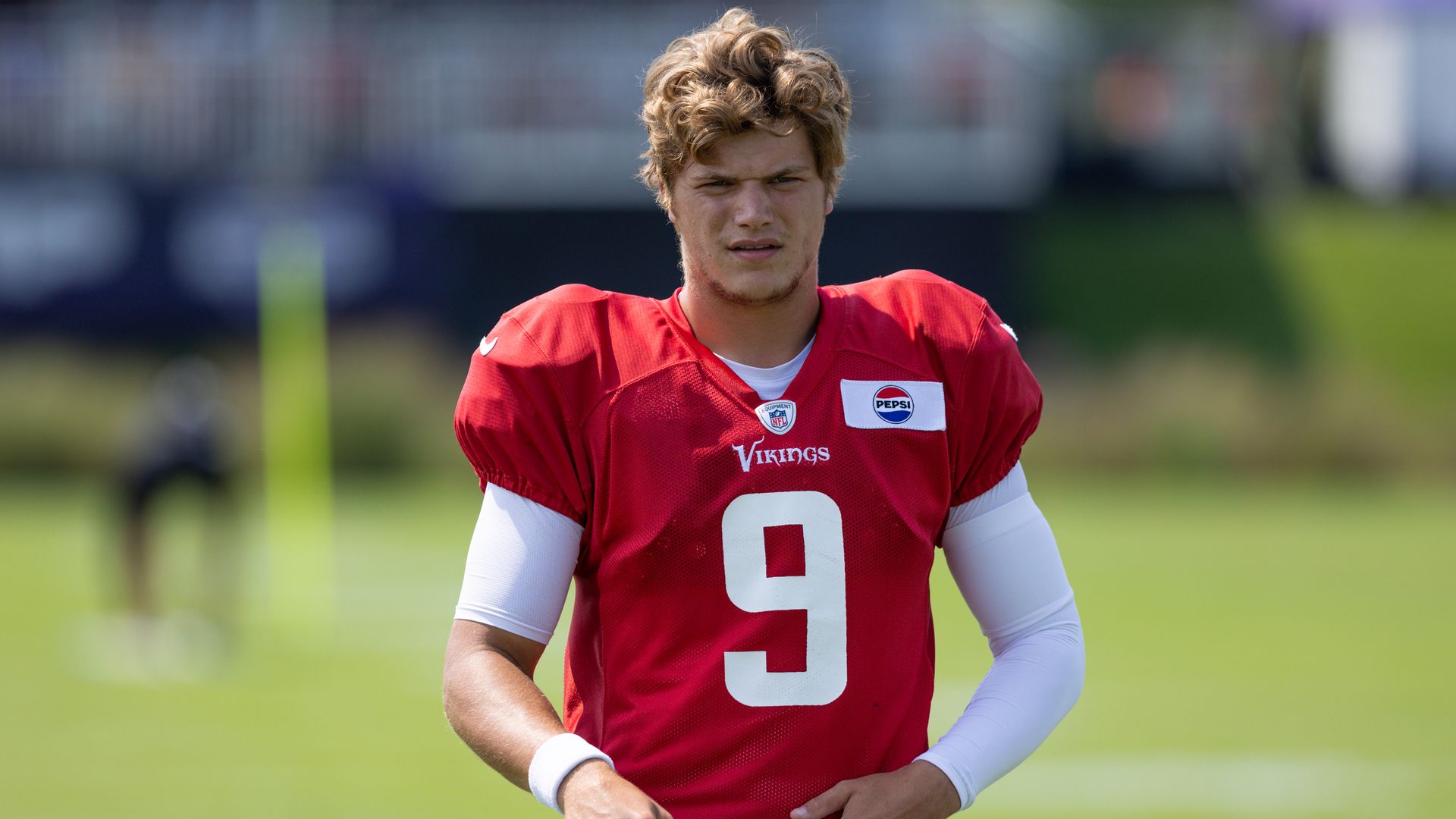 JJ McCarthy in a red jersey number 9 stands on a football field 