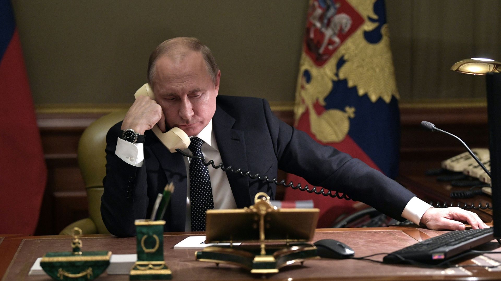 Photo of Vladimir Putin sitting at his desk holding a phone to his ear