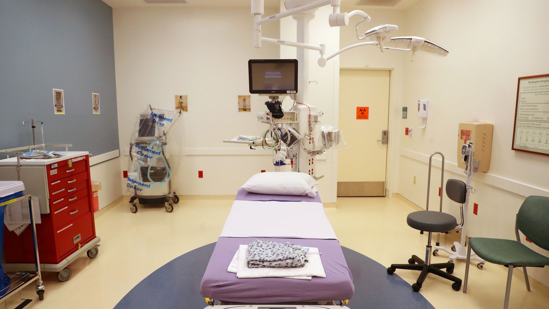 A beige hospital room with a bed, computer monitor and other health care devices.