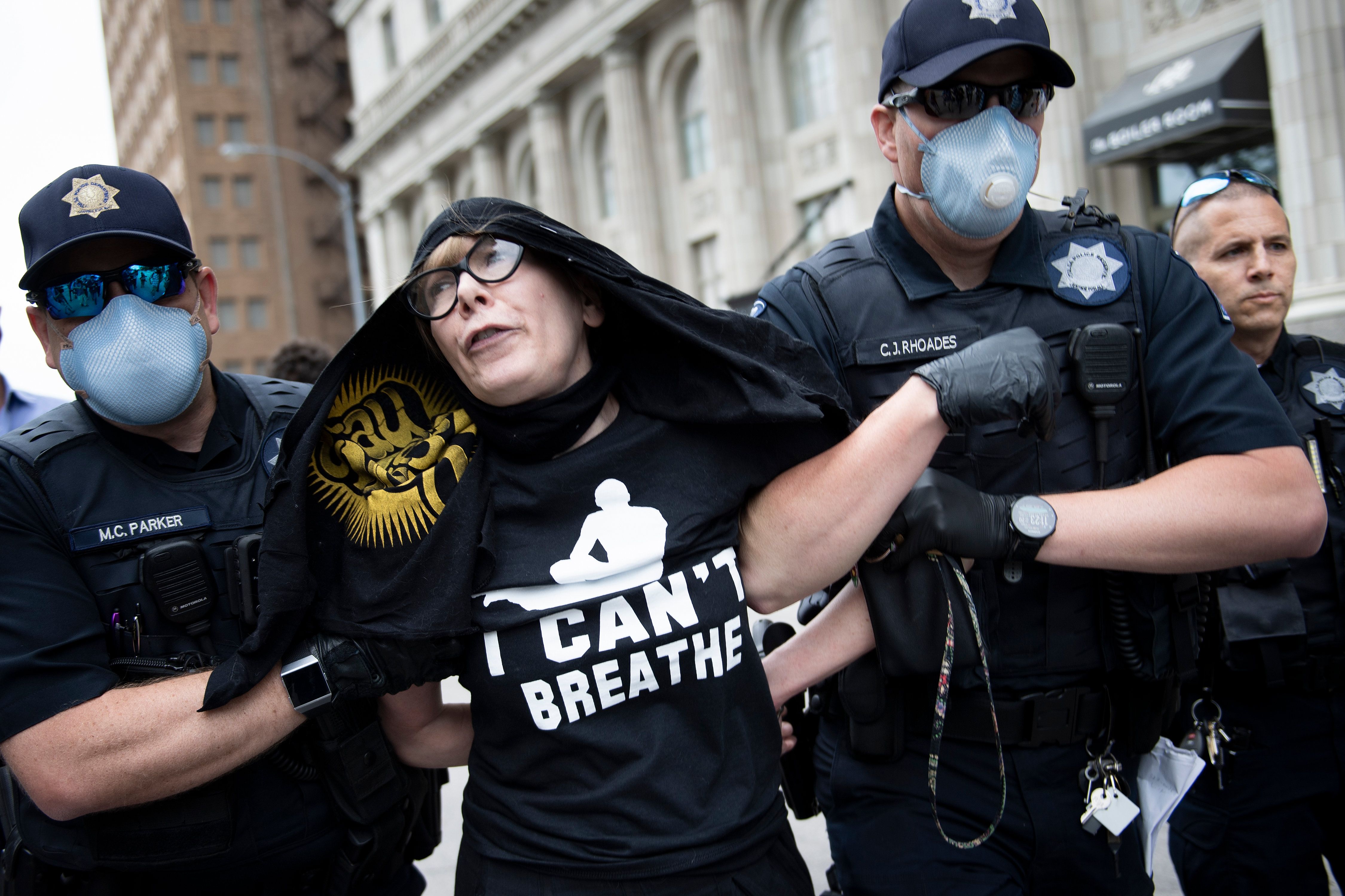 A woman wearing an "I can't breathe" shirt is carried by police wearing face masks