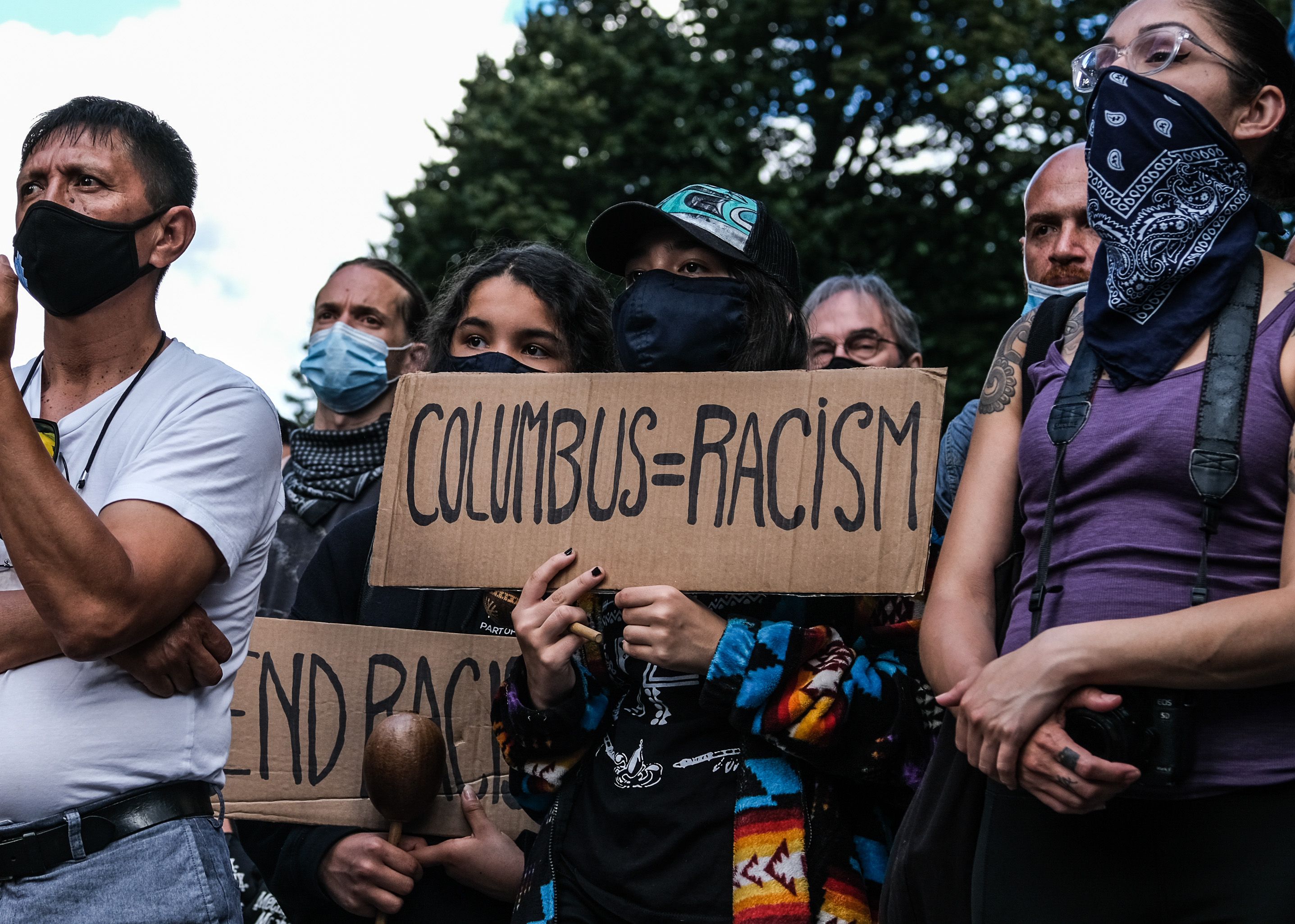 A cardboard sign reading "Columbus=Racism" held by protestors with the The Indigenous People's Day New York City Committee in New York City in 2020.