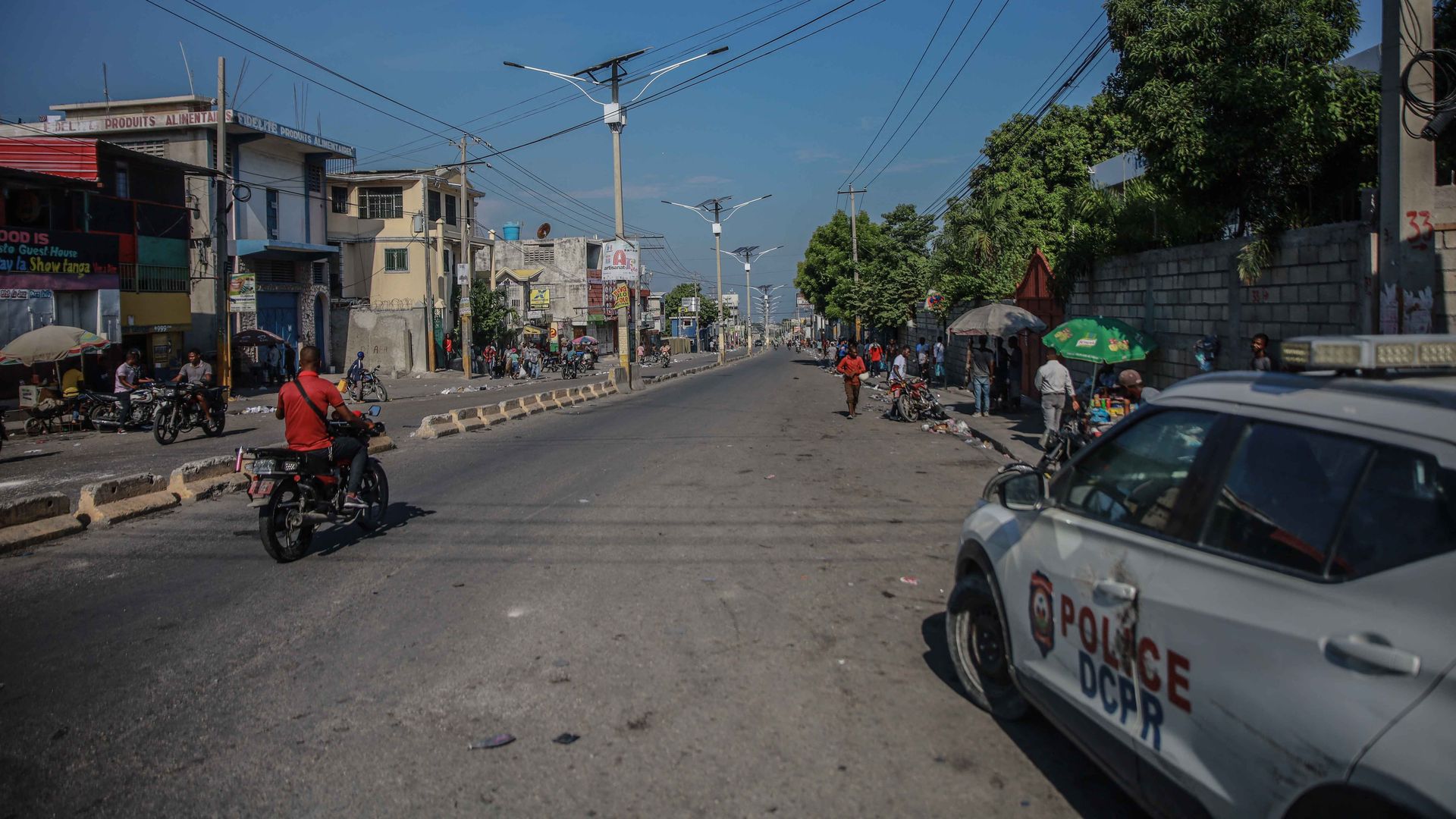 People ride a motorcycle past a police car following a call for a general strike launched by several professional associations and companies to denounce insecurity in Port-au-Prince
