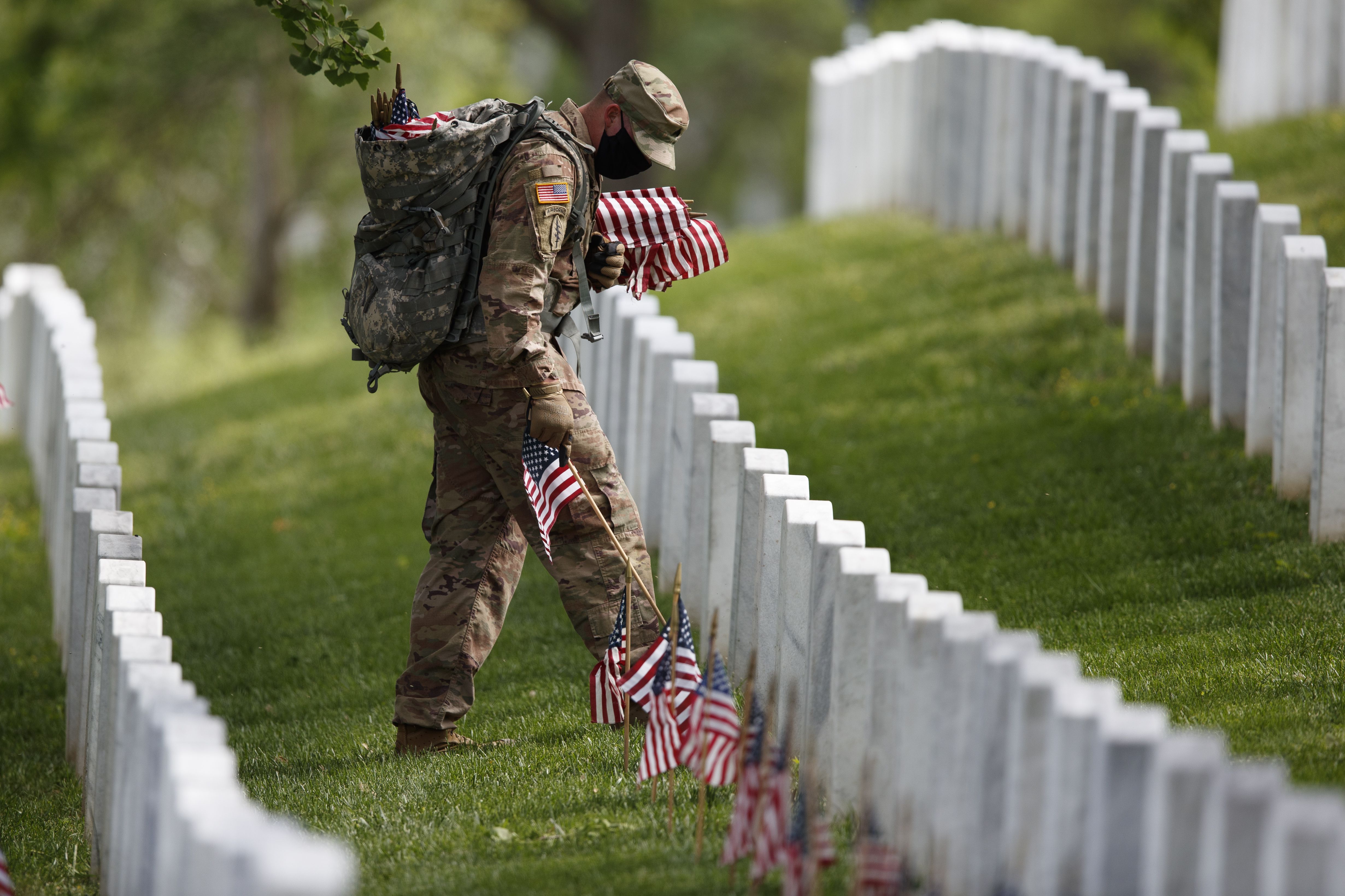 A uniformed soldier plants small American flags on graves 