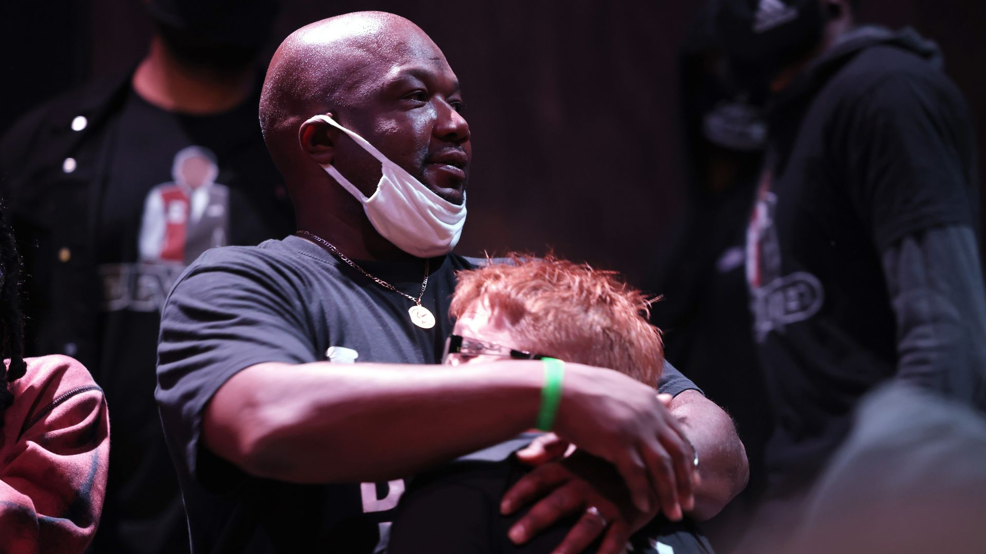 Image of a man hugging someone with red hair close to his chest while wearing a face mask 