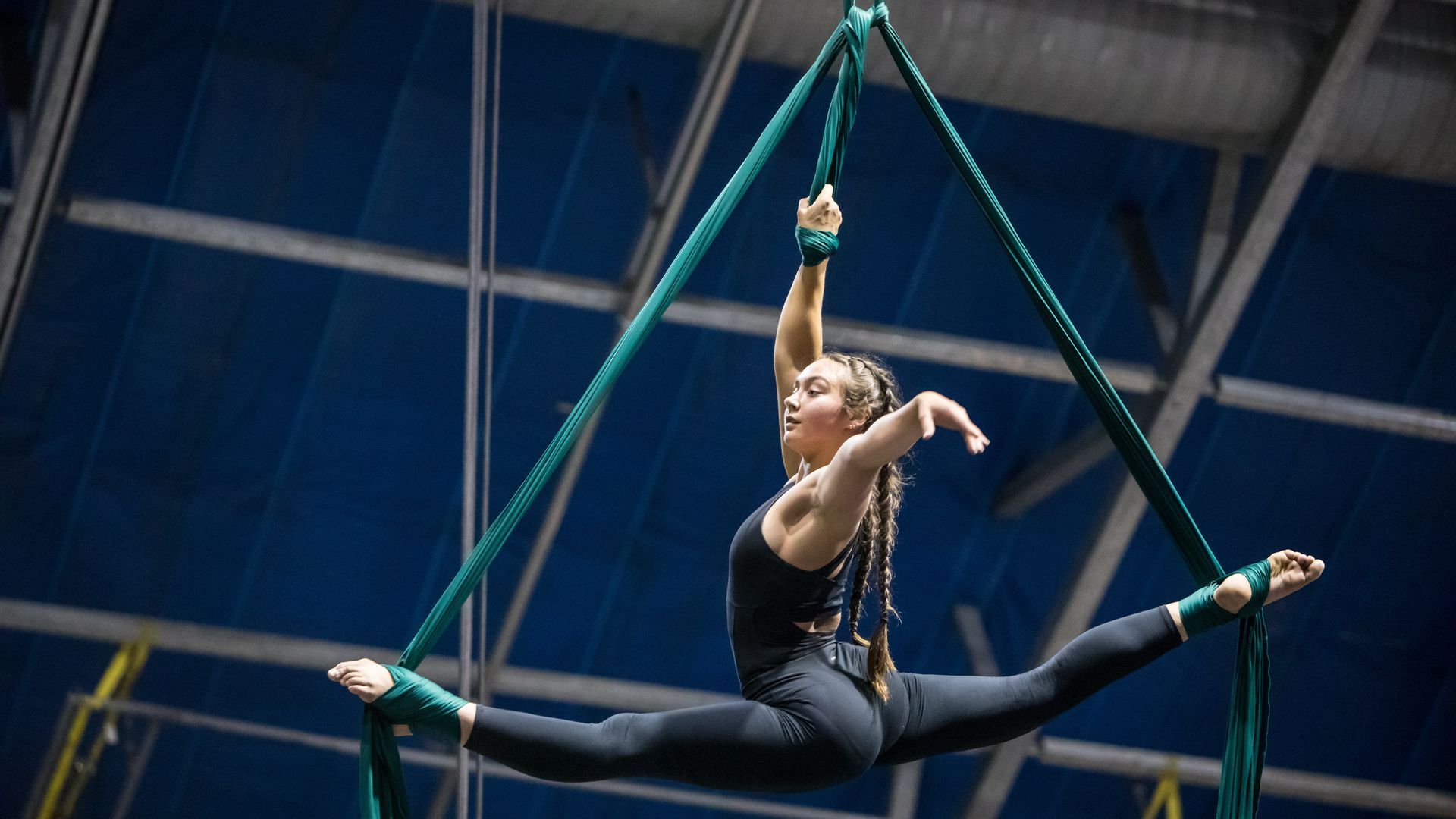 A photo of a young woman doing the splits in the air, wrapped in silk ropes.