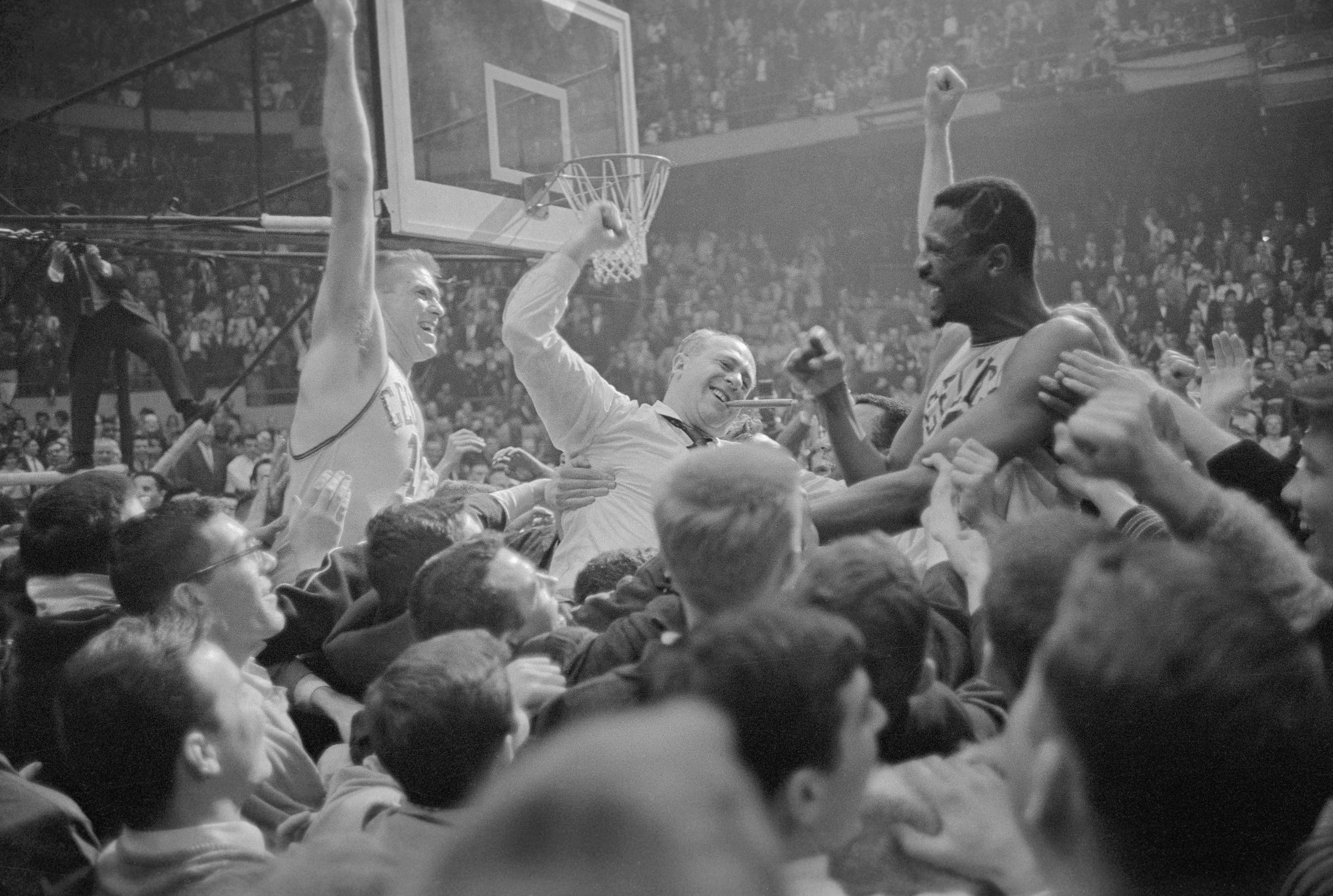Black and white picture of Bill Russell, Red Auerbach and Tommy Heinsohn being held up by a crowd and celebrating with their arms up