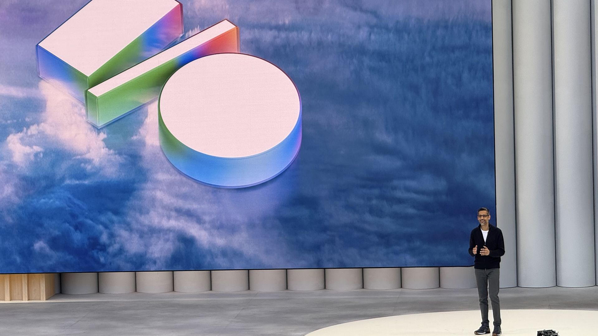 Photo of Google CEO Sundar Pichai standing on stage next to a projected Google I/O logo