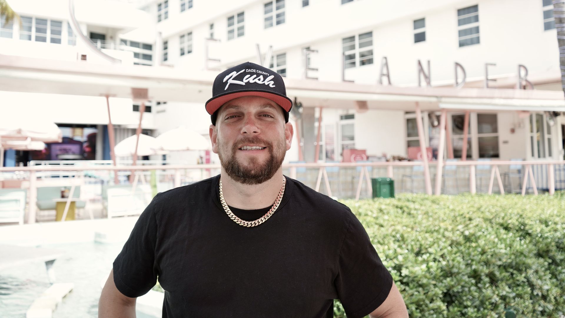 Matt "Kush" Kuscher stands in front of the Clevelander Hotel on a sunny day wearing a baseball cap that says "Miami." 