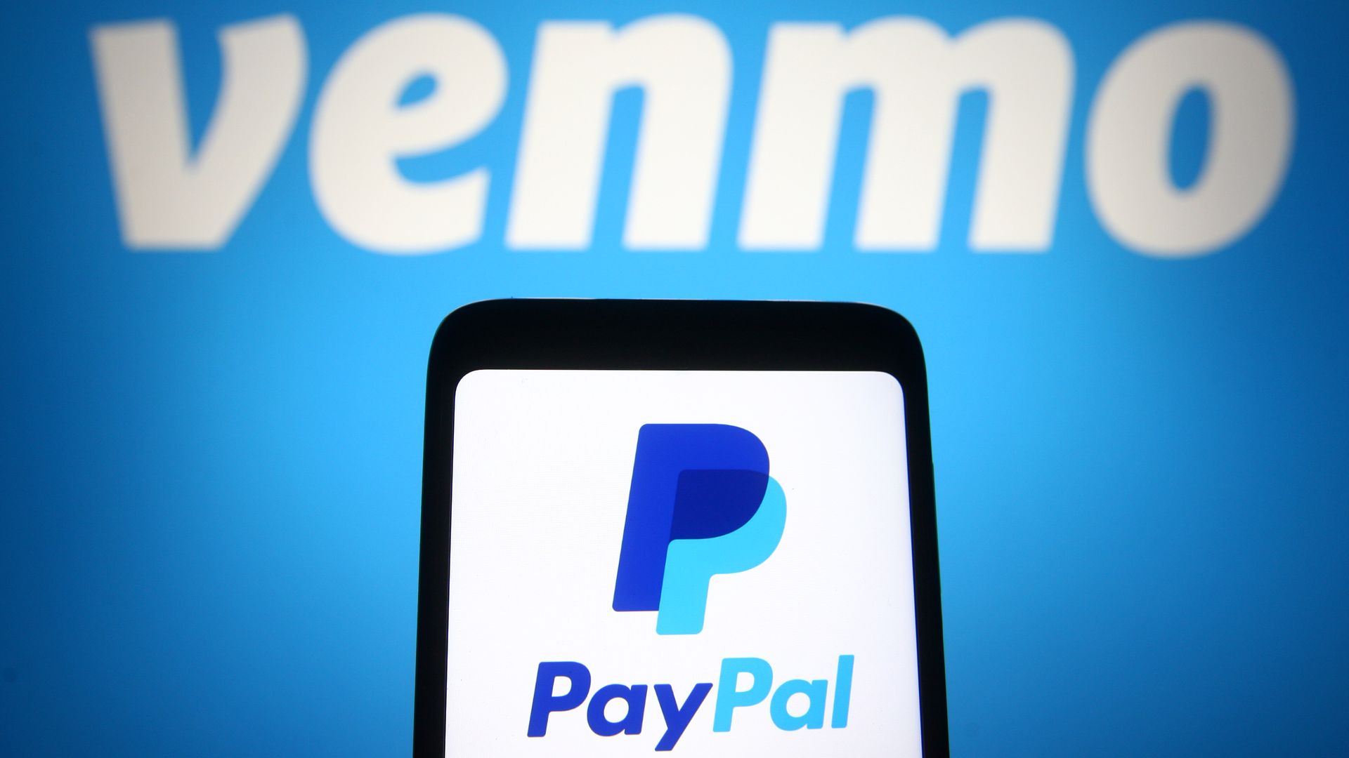 Close-up of a smartphone displaying the PayPal logo on its screen, set against a blue background with large, blurred white letters in the backdrop.