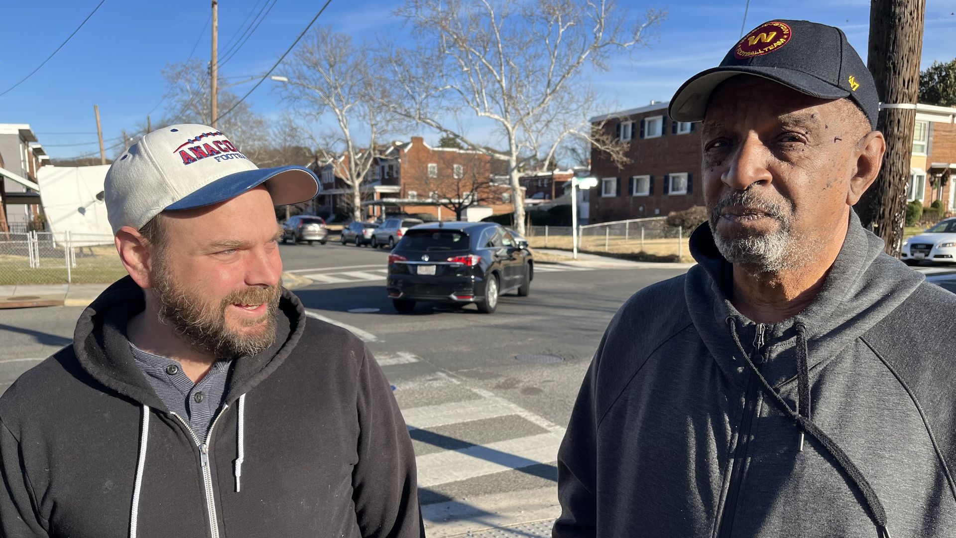 D.C. residents Nathan Luecking and Charles Lockett stand together on a front yard, with an intersection in the background. 