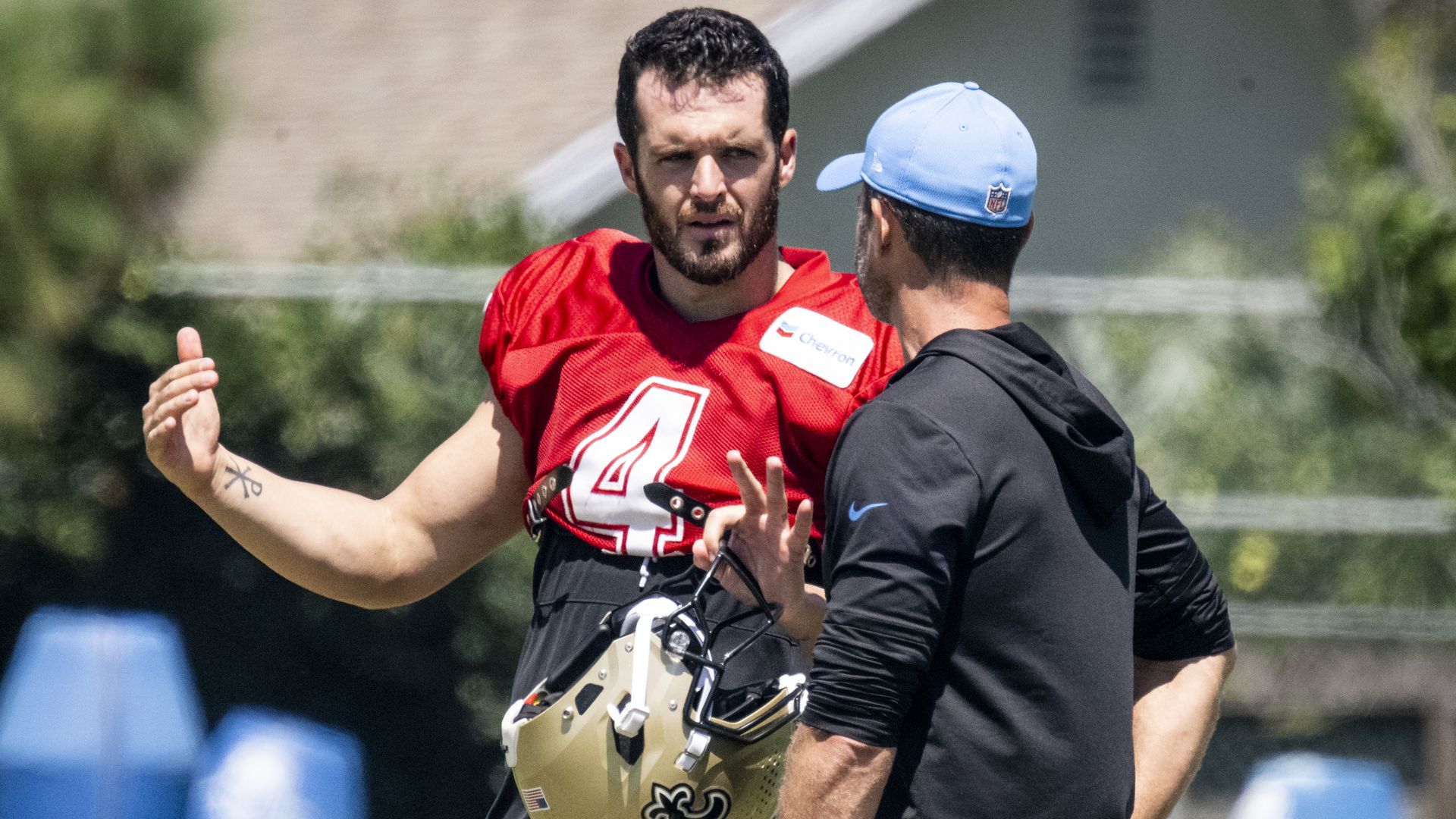 Derek Carr speaks with a Los Angeles Chargers head coach Brandon Staley during a training camp practice. Carr holds his football helmet in one hand.