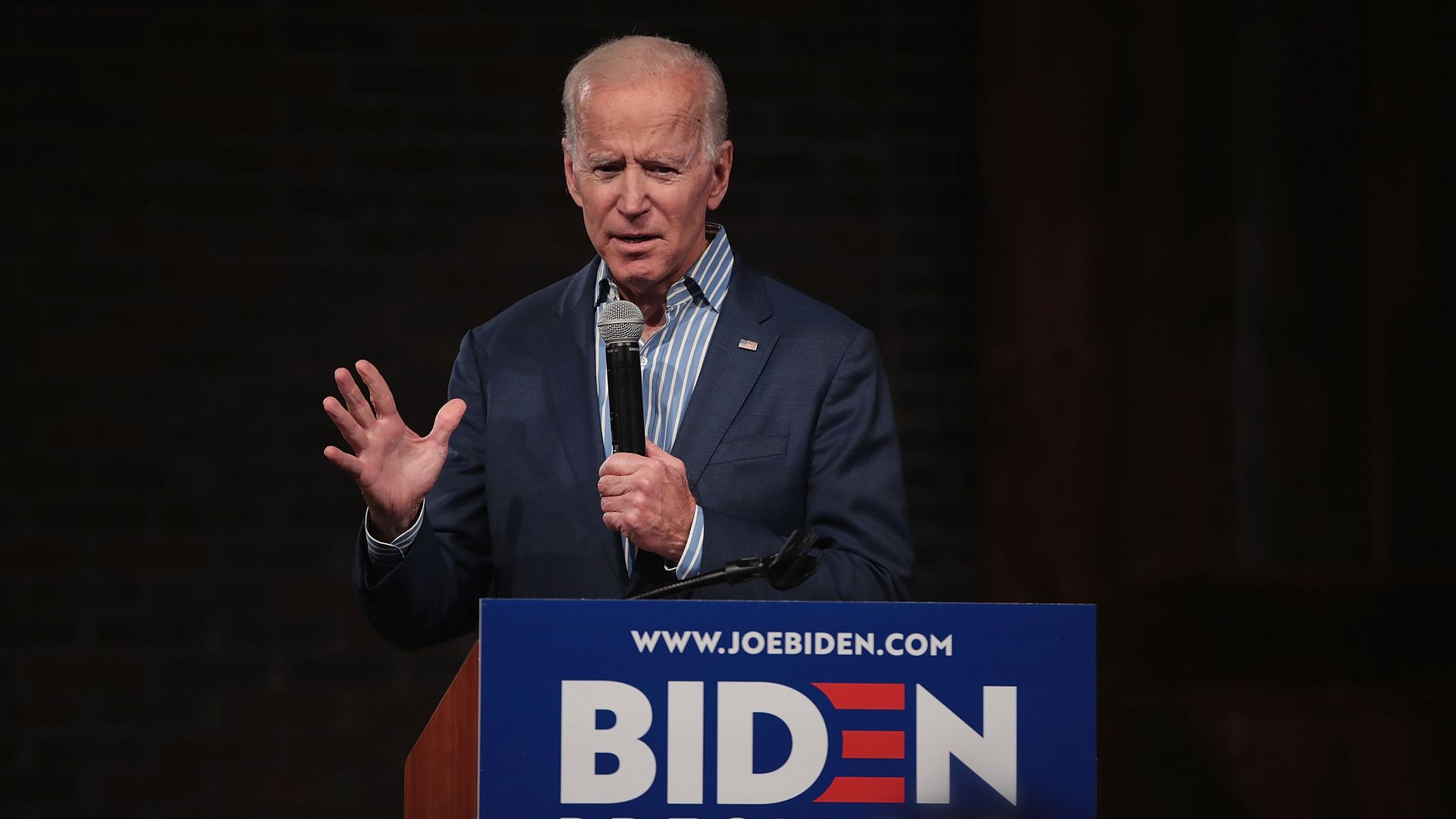 In this image, Biden stands behind a podium with his name on it and speaks into a microphone.