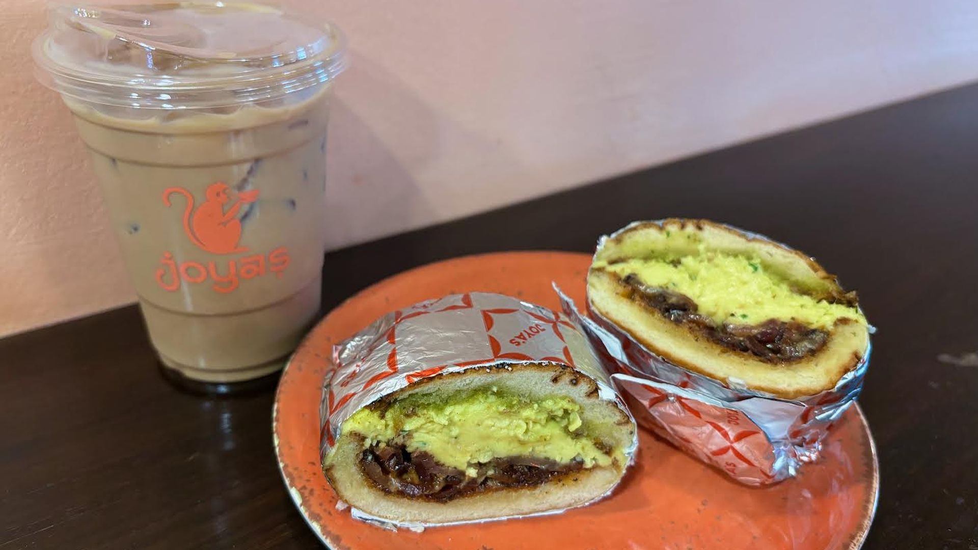A breakfast sandwich and an iced latte from Joya's on a table counter. 
