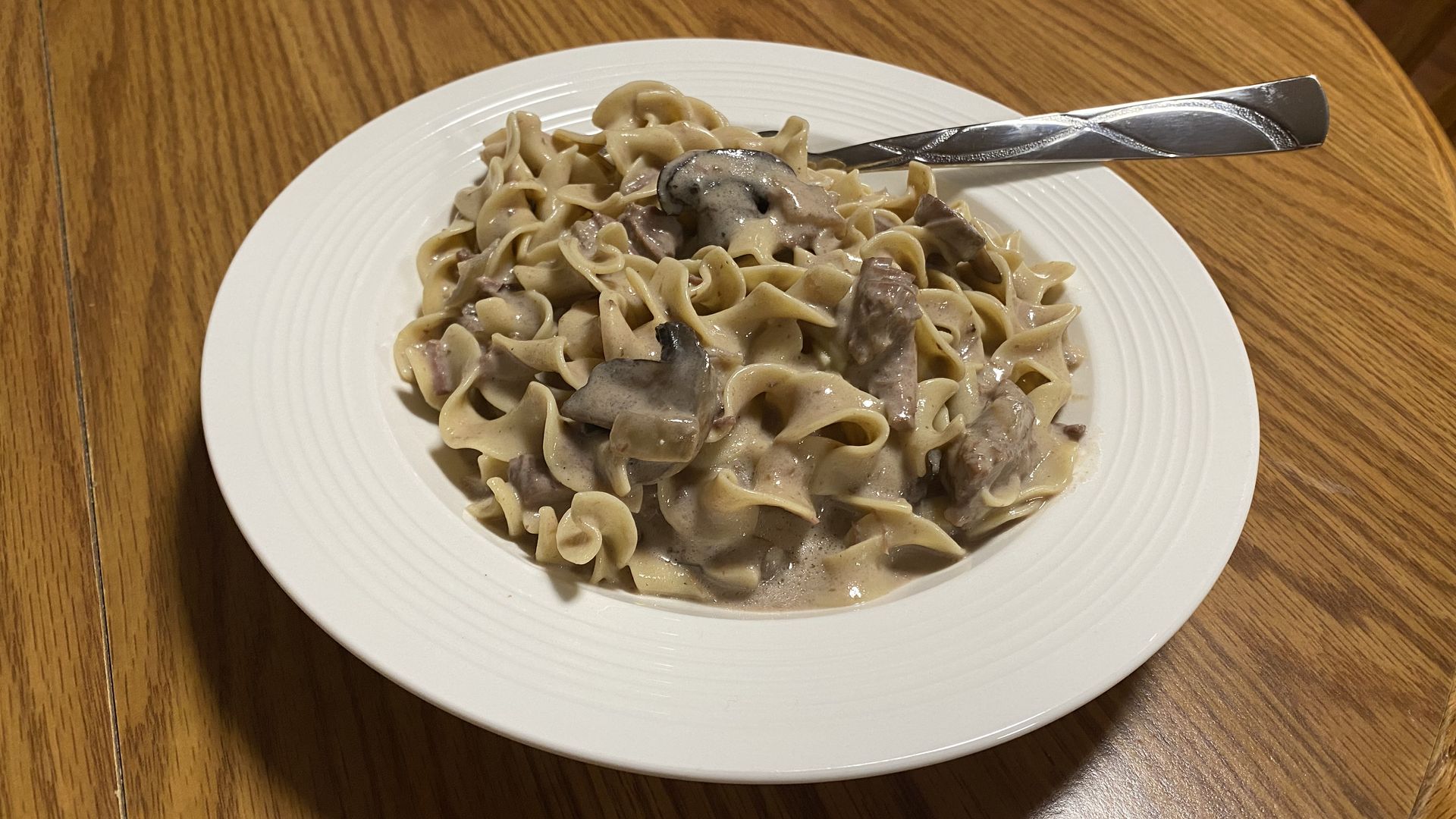 A white bowl of beef stroganoff with a silver fork