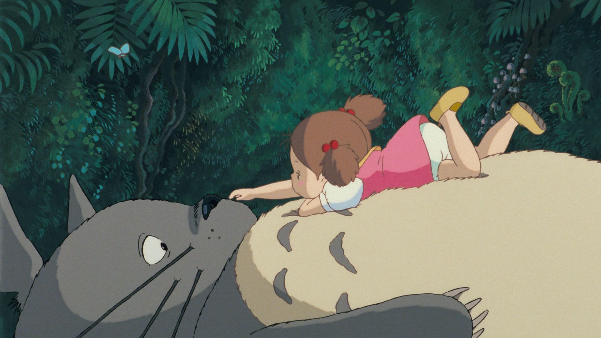 Still from the Studio Ghibli film "My Neighbor Totoro" with the character Mei sitting on Totoro and poking its nose