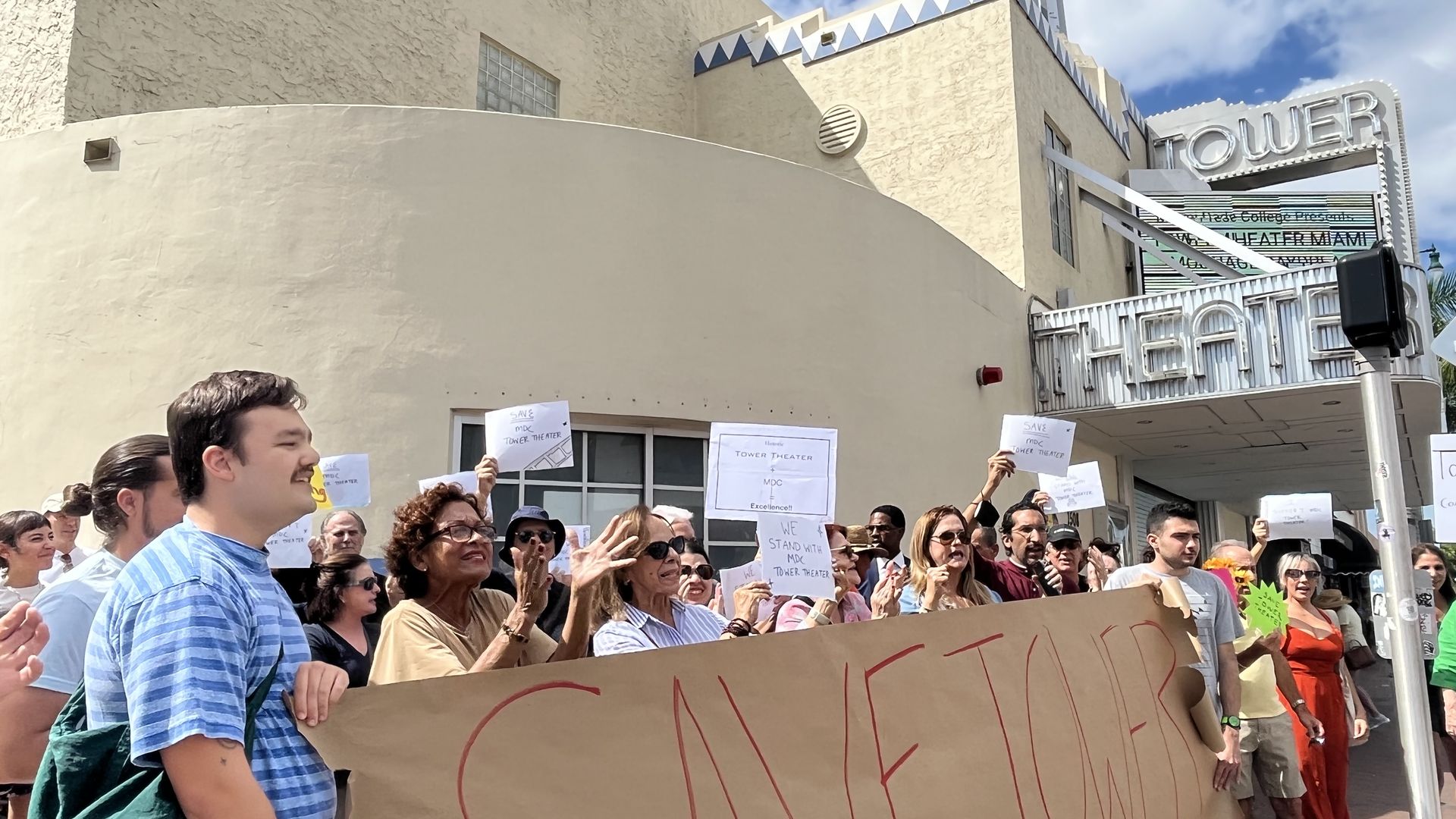 Protesters gather outside Tower Theater in Miami, waving signs and chanting.