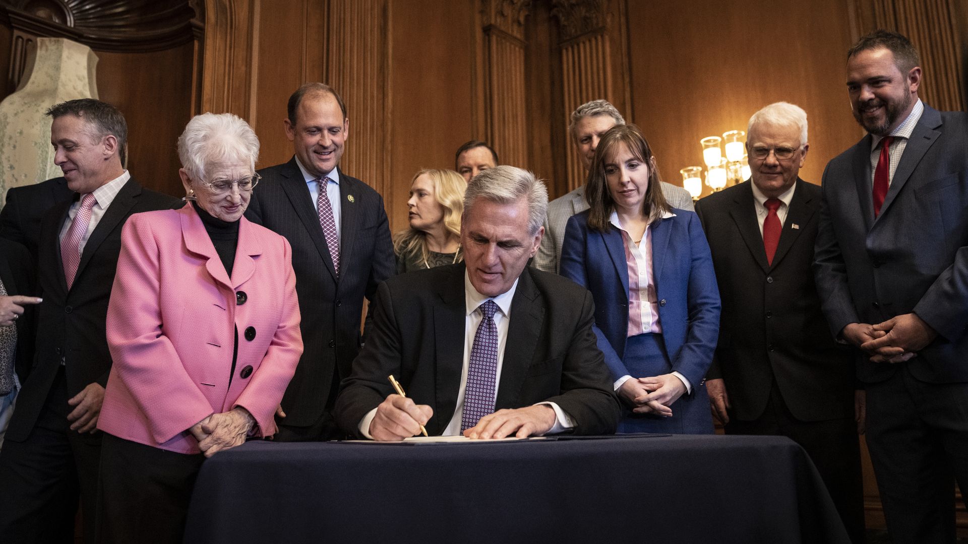 House Speaker Kevin McCarthy, wearing a dark gray suit, white shirt and purple time, enrolls an anti-ESG bill surrounded by colleagues and others.