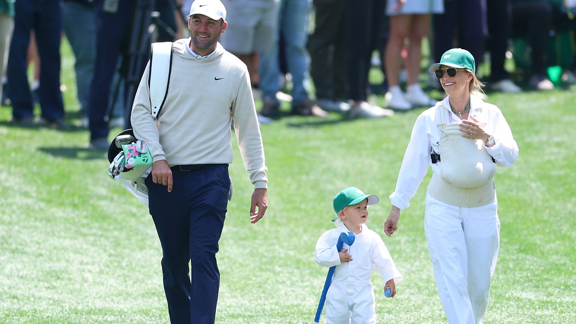 Scottie Scheffler, his wife Meredith and their sons Remy and Bennett walk on a green wearing golf gear