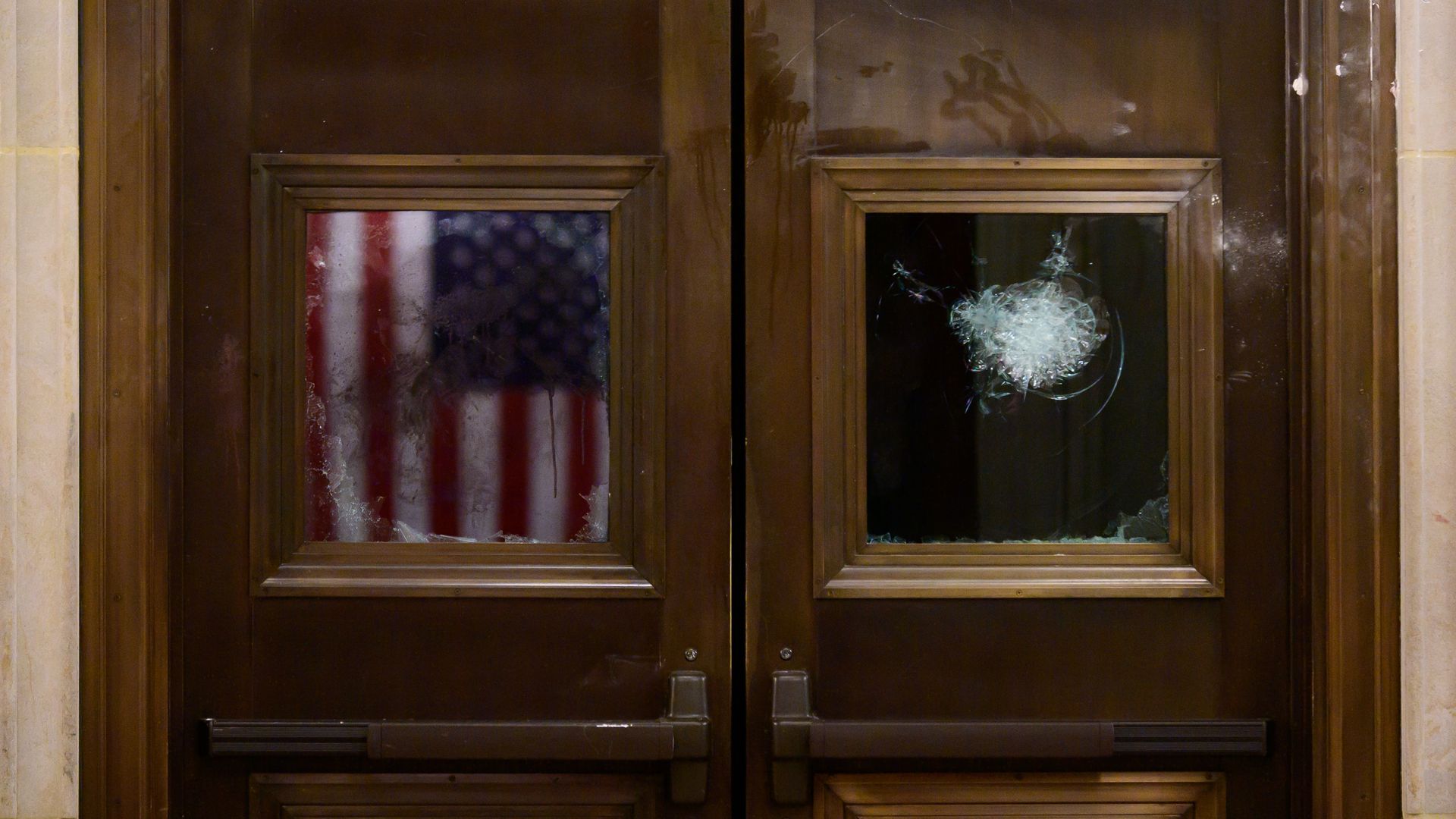 Photo of a door that shows an American flag through the glass on one side and a crack in the glass on the other
