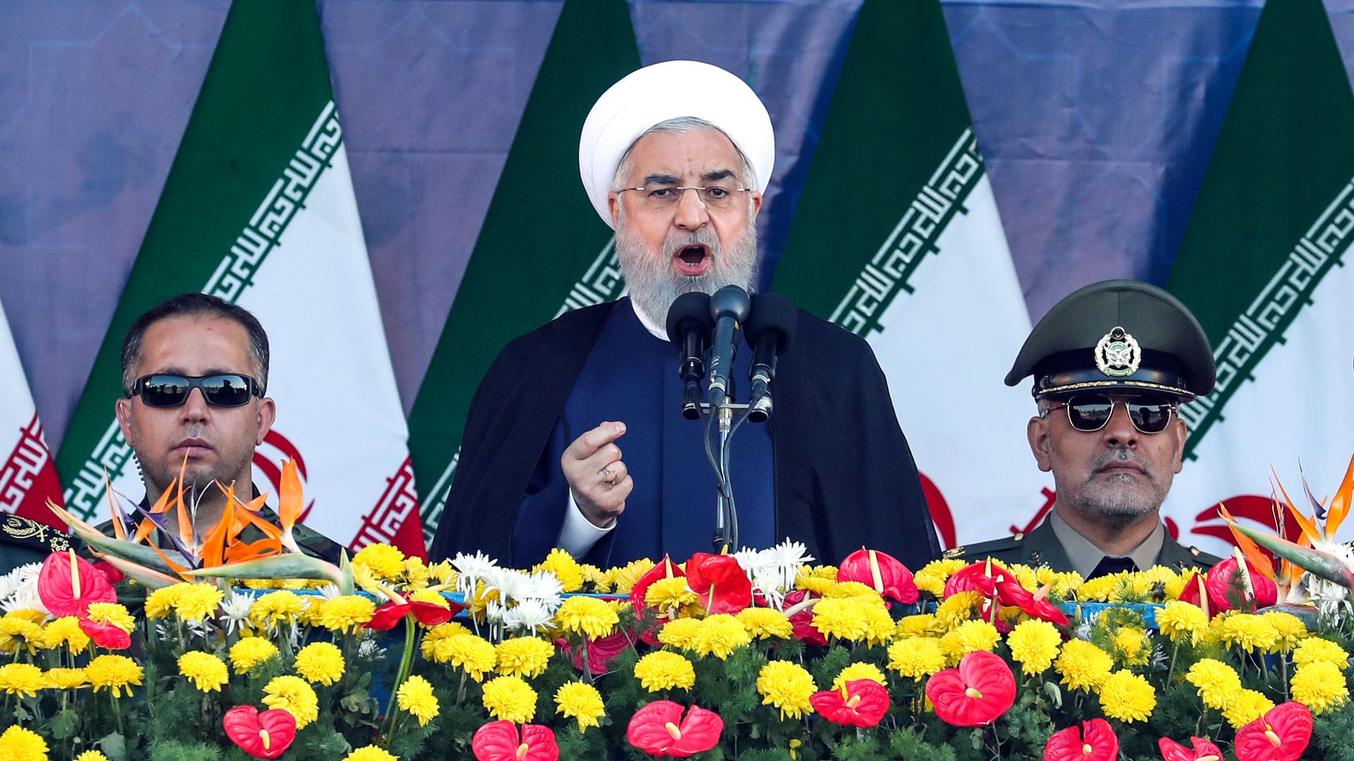 Iranian president giving a speech in front of a bed of flowers